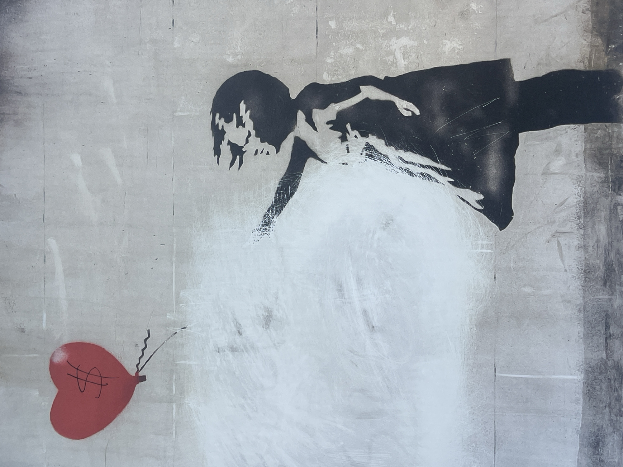 This vertical image captures a stencil artwork on a light grey concrete wall in Barcelona, Spain. The artwork depicts the silhouette of a young girl, rendered in black, positioned on the right side of the frame. She is facing towards the right, with her left arm extended upwards and slightly to the left, appearing to reach. The girl's form, including her dress and hair, shows variations in tone, suggesting stencil application marks or wear. In the upper left section of the image, a red, heart-shaped balloon is depicted, featuring a distinct black dollar sign ($) centrally on its surface. Two dark, thin, wavy lines trail downwards from the base of the balloon, resembling its strings. The concrete wall background exhibits horizontal seams and notable white paint streaks and patches, particularly dense in the mid-left area, partially obscuring the wall and the area around the girl's outstretched arm. Darker grime or discoloration is visible along the top edge of the wall, and the bottom quarter displays a darker, rougher texture, consistent with a lower wall section or ground level.