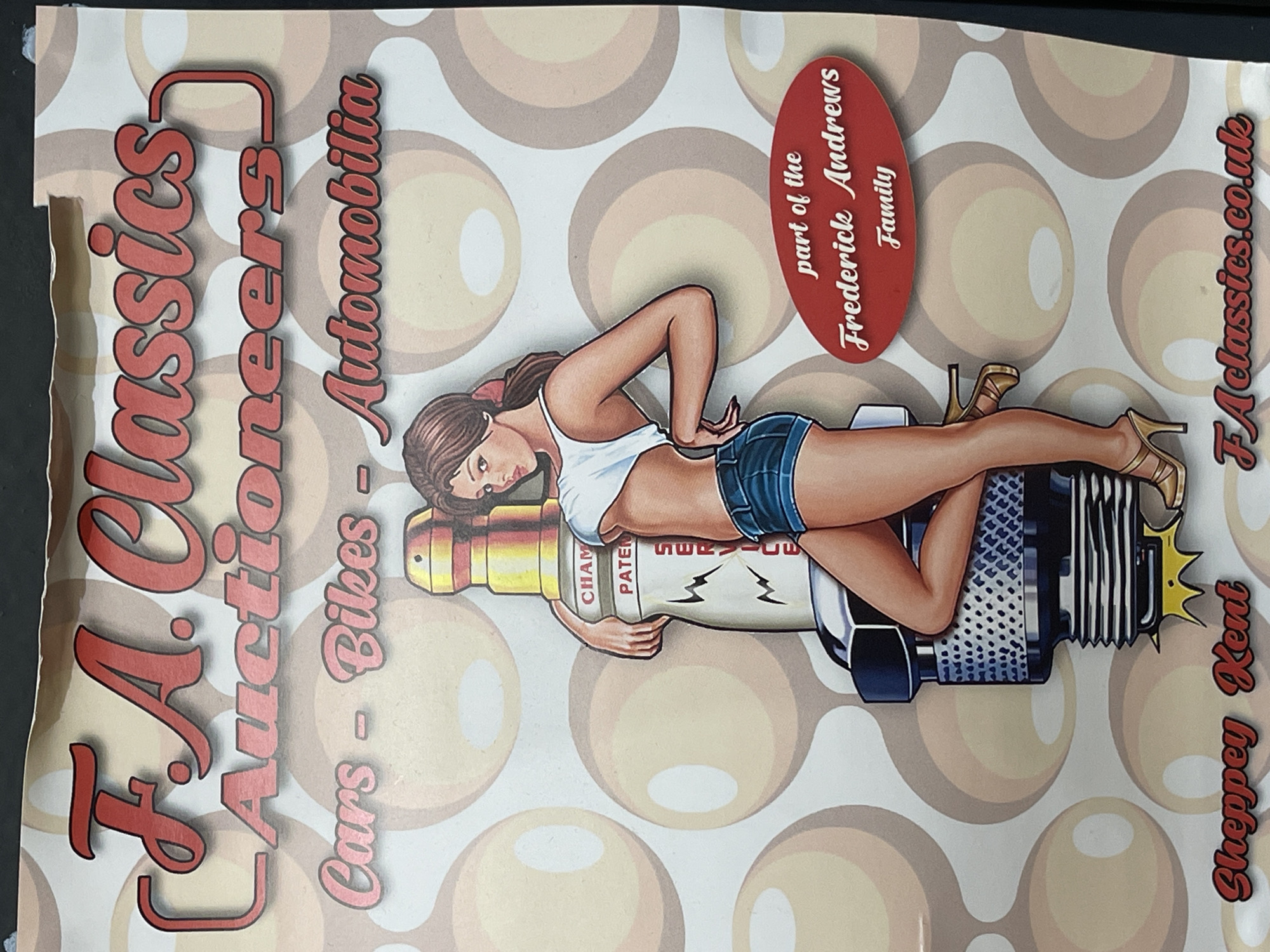 This media file is a vibrant, retro-styled promotional poster for "F.A. Classics Auctioneers," based in Sheppey, Kent, United Kingdom, which is near Maidstone. The central subject is a pin-up style illustration of a woman with brown hair, wearing a white crop top and denim shorts, posed suggestively on a large, stylized spark plug. Her legs are extended, wearing golden high-heeled shoes, with one arm resting on the spark plug and the other hand behind her back.
The background features a repeating pattern of concentric circles and solid-colored spheres in shades of beige, brown, and off-white, contributing to the retro aesthetic. The spark plug itself has partial words visible, including "CHAM," "PATER," and "SERVI," likely referencing "Champion Patents Service" or similar spark plug branding.
Prominently displayed text on the poster reads "F.A. Classics Auctioneers," positioned vertically on the left side with a red, shadowed font. Below this, "Cars - Bikes - Automobilia" indicates the types of items auctioned. A red oval badge on the right proclaims "part of the Frederick Andrews Family." At the bottom right, "Sheppey Kent" specifies the location, and "FAclassics.co.uk" provides the website. The overall impression is a blend of classic automotive culture with nostalgic pin-up art, promoting a family-run auction business specializing in vehicles and automobilia. No specific time of day or weather is indicated.