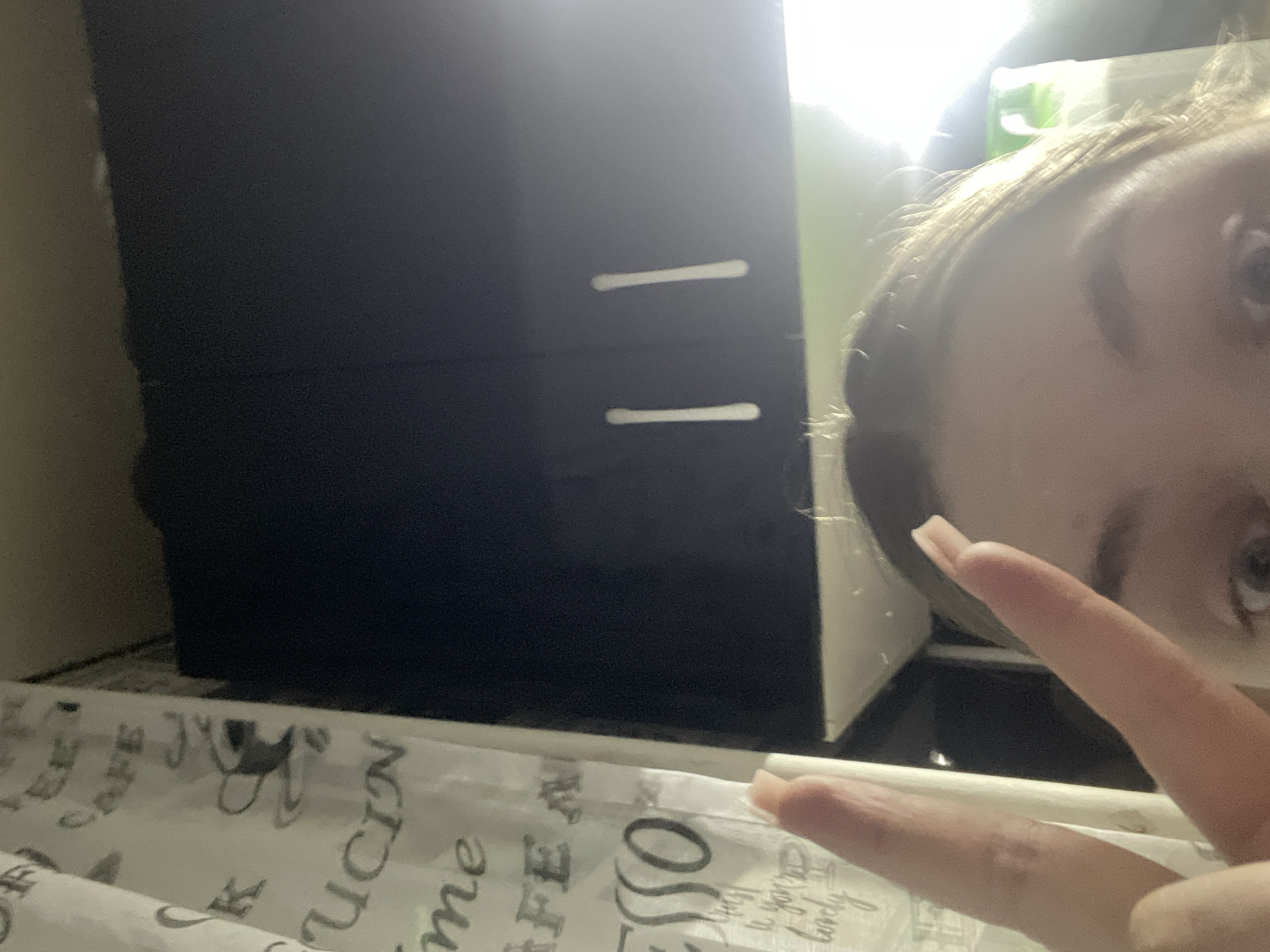 The image shows a person's face and hand in the foreground. In the background, there is a dark-colored dresser or cabinet with two drawers, and a white surface with coffee-themed text. The location of Chaikovsky, Russia is not confirmed and cannot be determined from the contents of the image.
