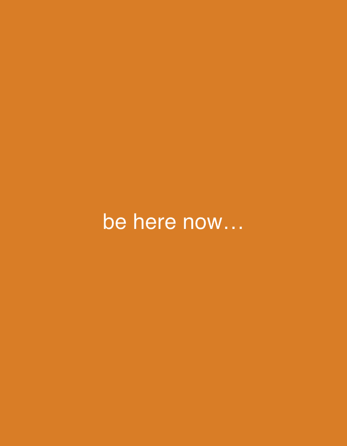 The image displays the phrase "be here now..." in white text centered on an orange background. The location is not evident from the image.