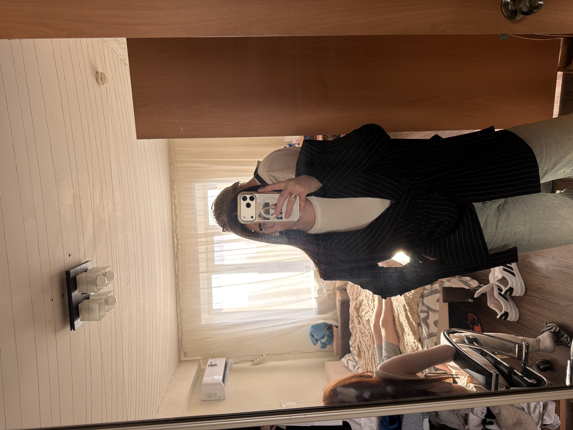A person takes a selfie in a mirror. The reflection shows a room with a window, bed, and clothes rack. The room is presumed to be in Izhevsk, Russia, based on the user's city information.