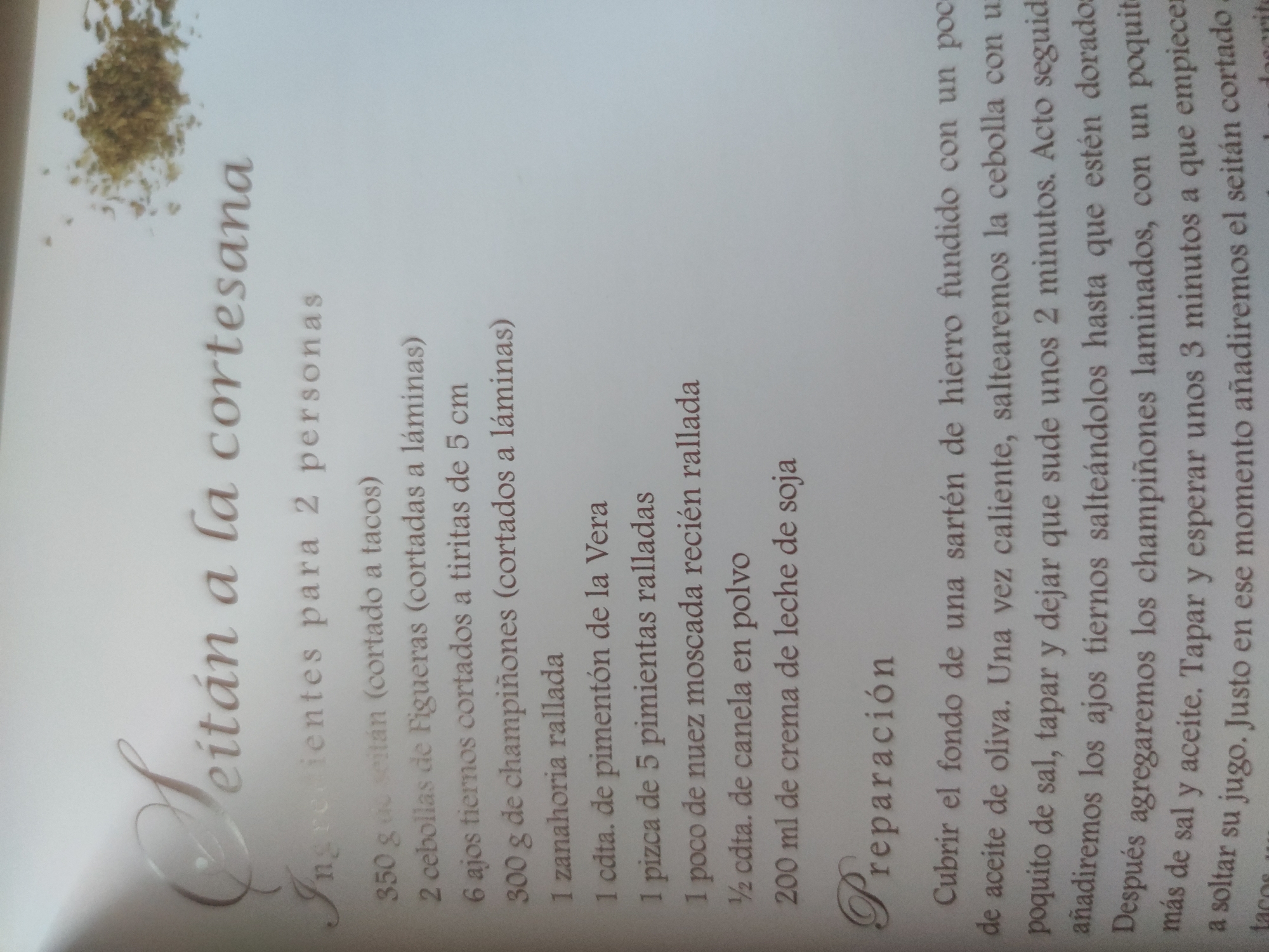 The image shows a page from a cookbook with a recipe titled "Seitán a la cortesana" (Seitan in the style of the court). The recipe is for two people and lists ingredients such as seitan, Figueras onions, garlic, mushrooms, carrots, pimentón de la Vera, pepper, nutmeg, cinnamon, and soy cream. The preparation instructions describe how to sauté the ingredients in a cast iron skillet.