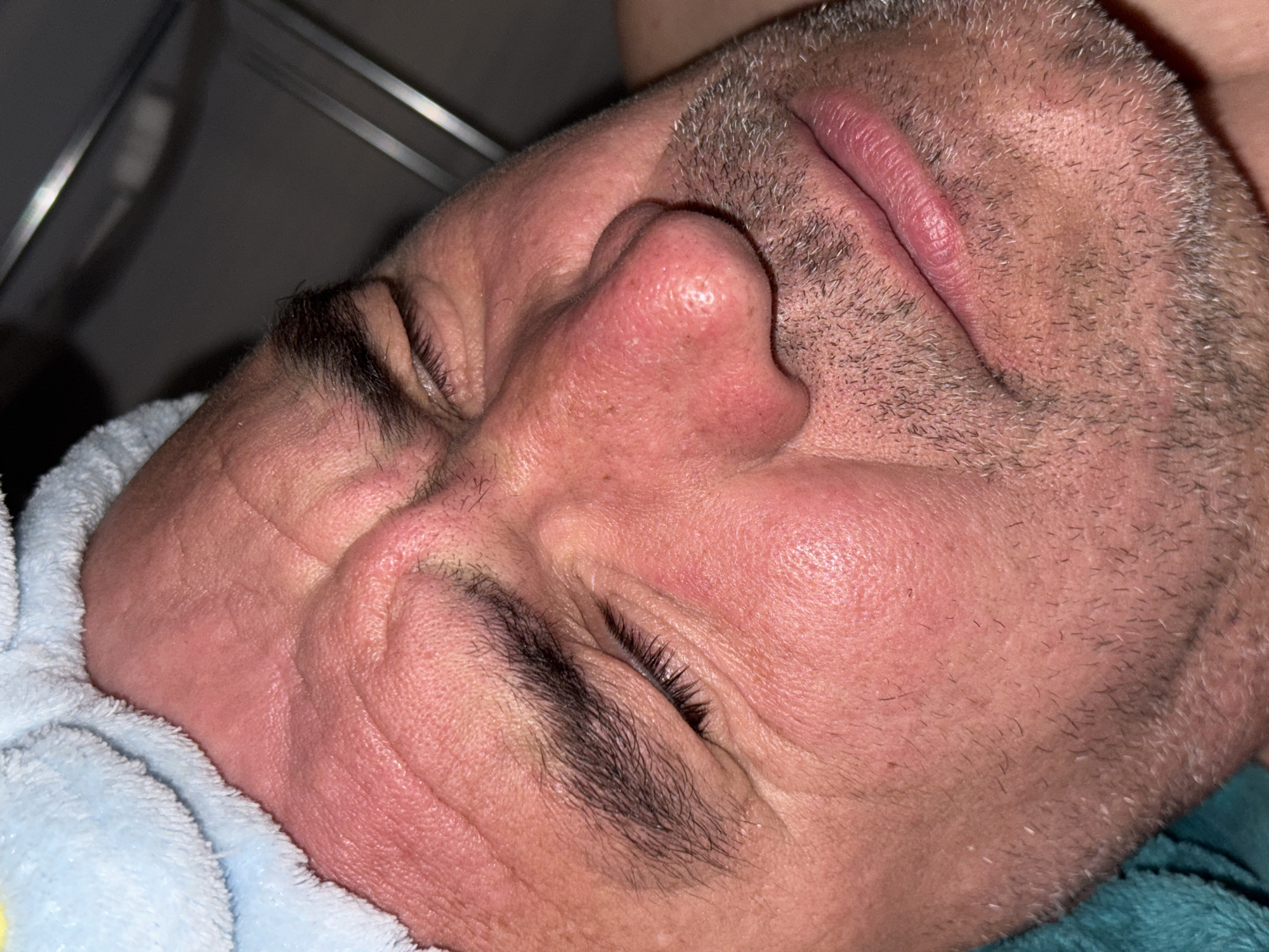 A close-up image shows a man's face resting on a blue and white towel. His eyes are closed and his expression appears relaxed. The image does not include any information relating to the city of Vladivostok, Russia.