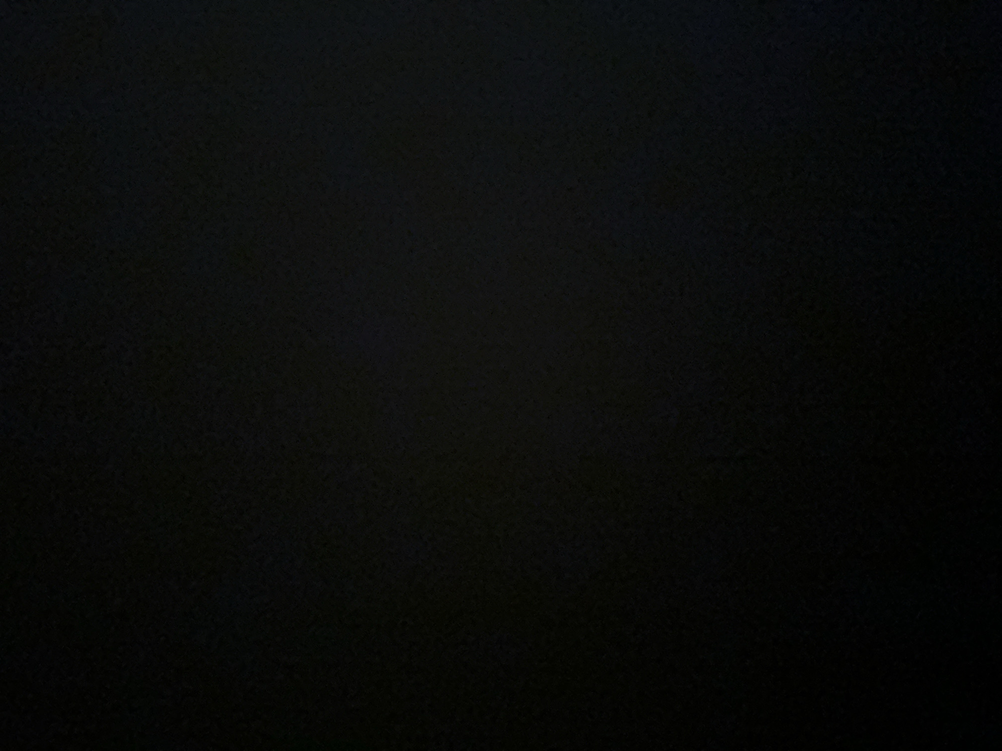 This is a dark, abstract image with no discernible subjects, objects, scene, setting, or activity. The entire frame is filled with a black or very dark gray background that has a textured appearance, suggesting it might be a surface like fabric or paper. There are no visible details indicating the time of day, weather, location, or emotions. No text is present in the image. The provided crops offer no additional information or clarity.