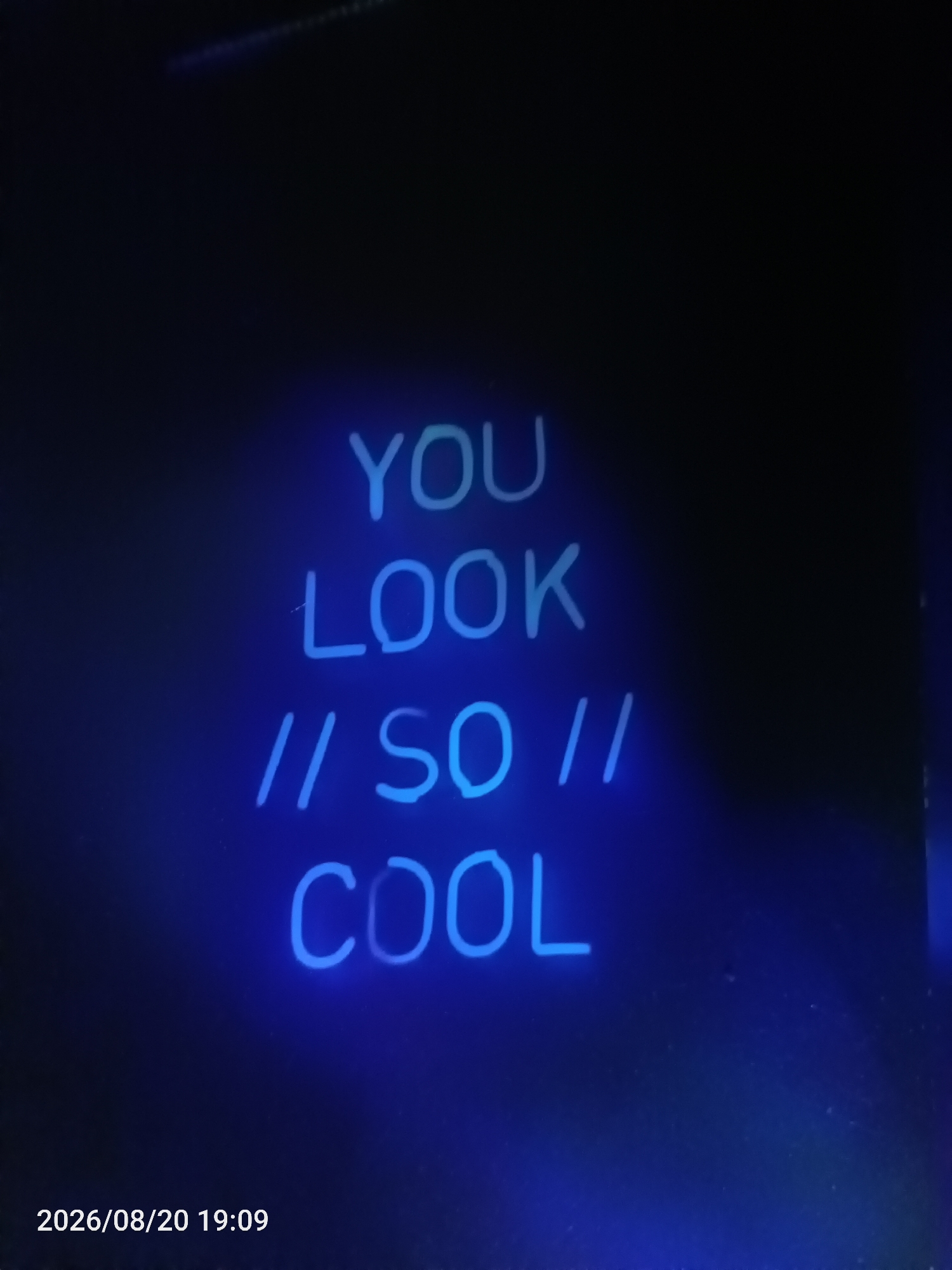 The image shows blue neon lettering on a black background. The text reads "YOU LOOK // SO // COOL". The bottom left corner of the image contains a timestamp that reads "2026/08/20 19:09". The image is of the city of Jawilan, Indonesia.