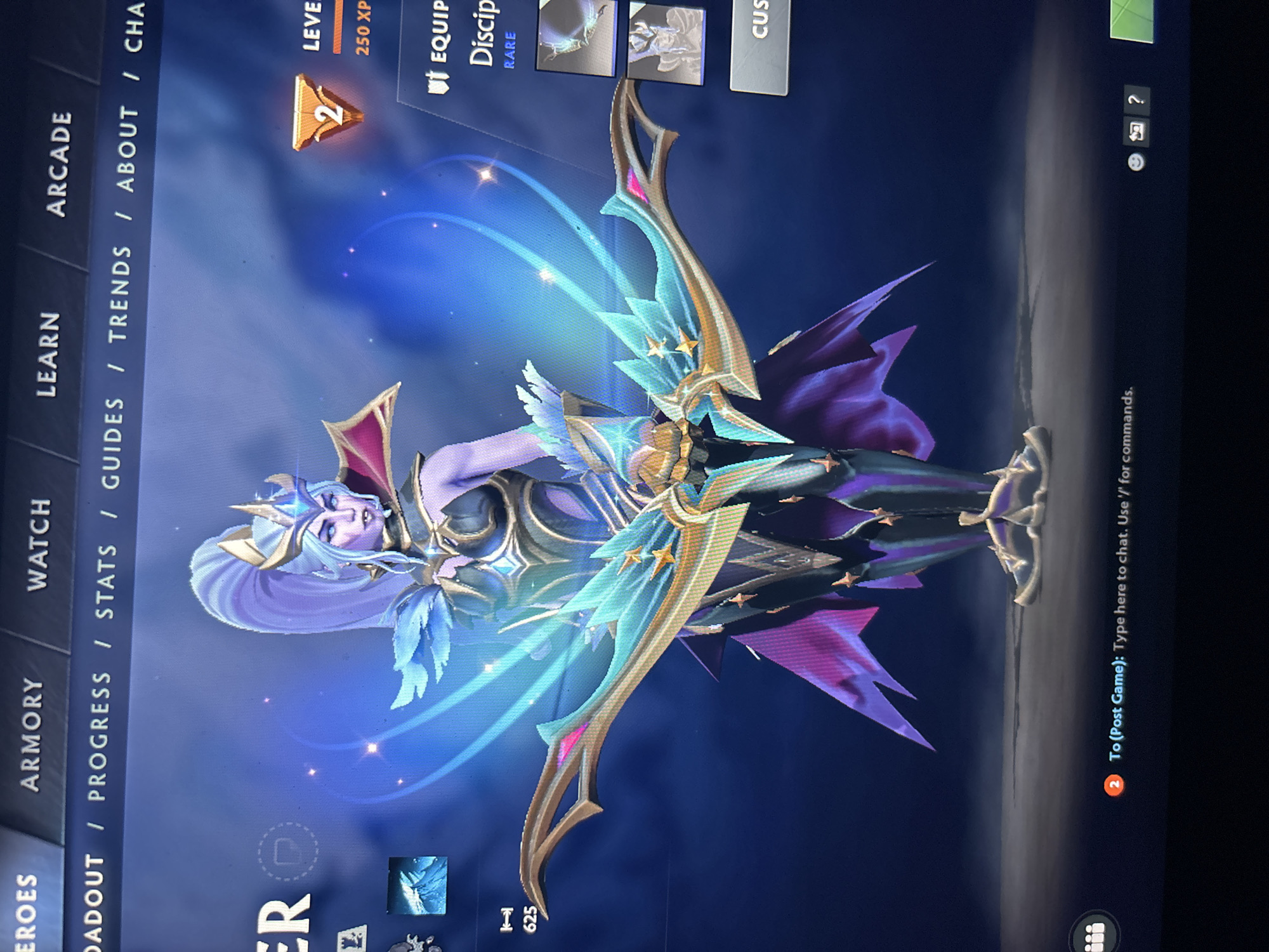 The image, captured in Sofia, Bulgaria, displays a vertical photograph of a video game screen. The central subject is a female fantasy character, likely an archer, standing in an ornate, heroic pose. She possesses long, light purple hair, a golden crown, and an elaborate costume featuring blue feathery shoulder pads, a gold and dark-colored bodice, and dark purple skirt-like elements. Her expression is calm yet determined. She holds a large, stylized bow that glows with bright blue energy streaks and is adorned with golden stars and light blue accents.
The character is presented within a game's user interface, suggesting a hero customization or selection screen. A vertical menu on the left side of the screen reads: "HEROES", "ARMORY", "WATCH", "LEARN", and "ARCADE". A horizontal menu across the top includes: "LOADOUT", "PROGRESS", "STATS", "GUIDES", "TRENDS", "ABOUT", and "CHA" (likely "CHAT").
Notable details from the interface include a "LEVEL 2" indicator with "250 XP" visible above the character. To the right of the character, under an "EQUIP" header, text reads "Discip" and "RARE", with small thumbnail images of equipable items. A button labeled "CUS" (likely "CUSTOM") is also present. Below the bow, the number "625" is visible. In the bottom right corner, a chat box displays: "2 To (Post Game): Type here to chat. Use '/' for commands." Above the chat box, small icons for help (question mark), replay, and a speaker are visible. The background of the game screen is a gradient of dark blue and purple, creating an ethereal atmosphere around the character.