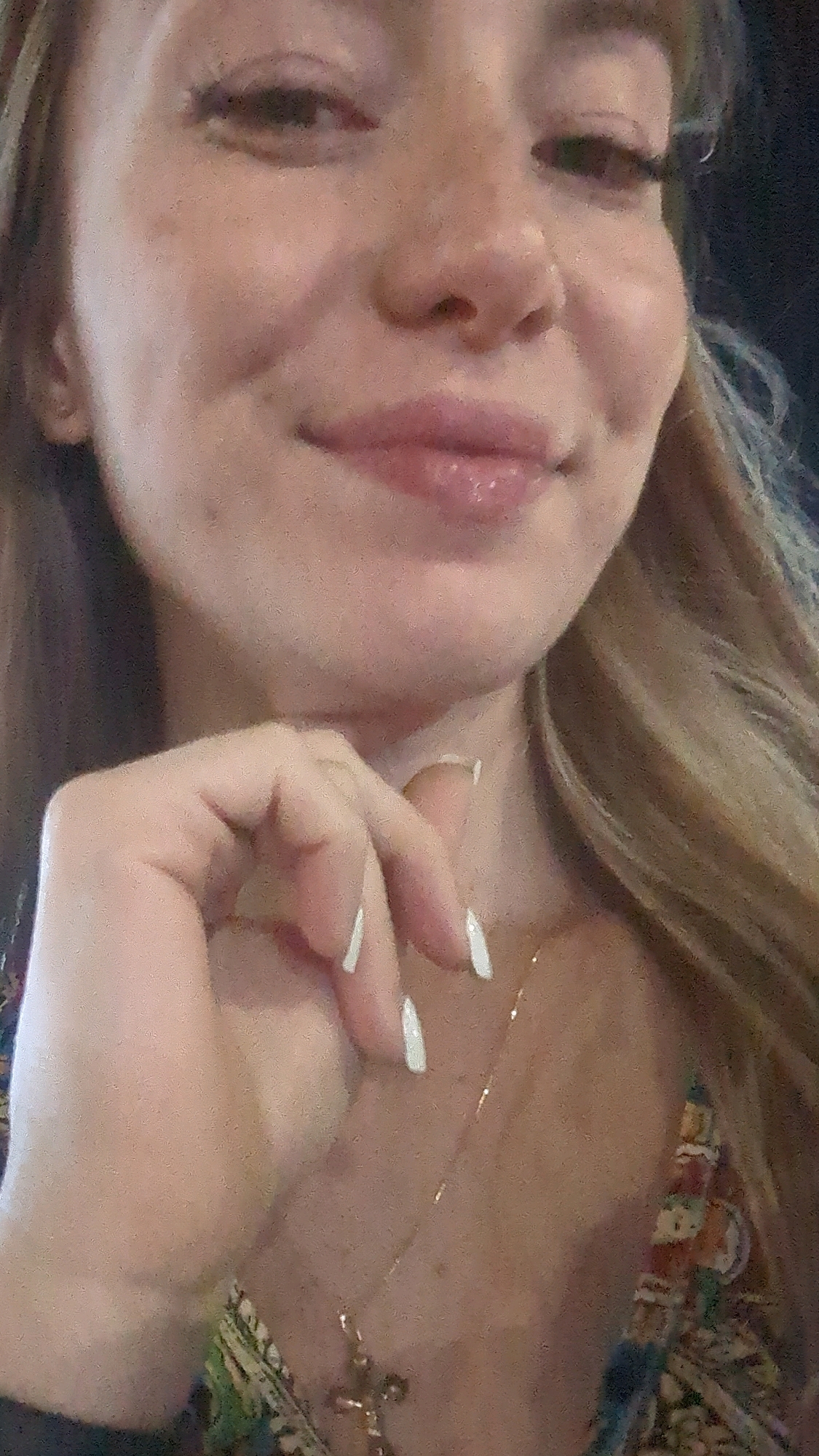 The image is a close-up, candid portrait of a young woman. Her face is partially visible, with her mouth slightly open, and her hand resting on her chin. She has blonde hair and fair skin with freckles. She is wearing a necklace with a cross pendant. The background is blurred and out of focus, suggesting a casual setting. There is no indication of the location within Chișinău, Moldova, nor any specific details about the environment that would allow for its identification. The image does not contain any discernible details that would allow for a forensic analysis of the scene.