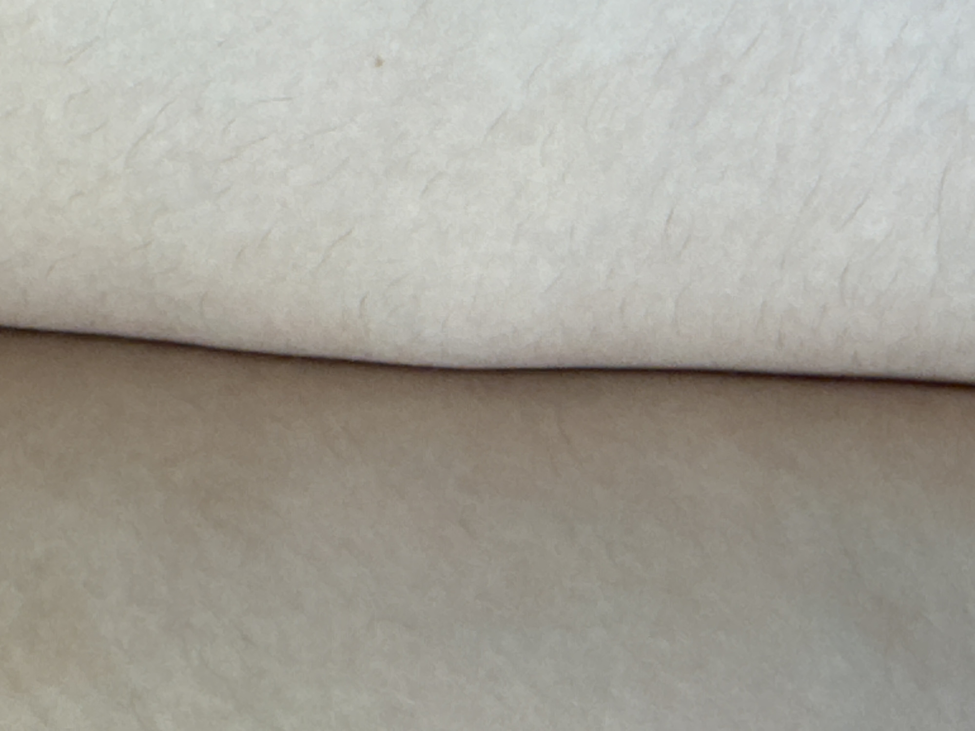 The image shows a close-up of two surfaces, likely paper or fabric, that are pressed together. The surface on the left is a uniform light brown, while the surface on the right is a lighter, off-white color with subtle variations in texture and some thin, faint lines. The two surfaces meet in the center, forming a soft crease. There is no indication of the city of Tolyatti, Russia, or any other specific location. The image is devoid of any people, objects, or actions that would suggest a particular scene or context.