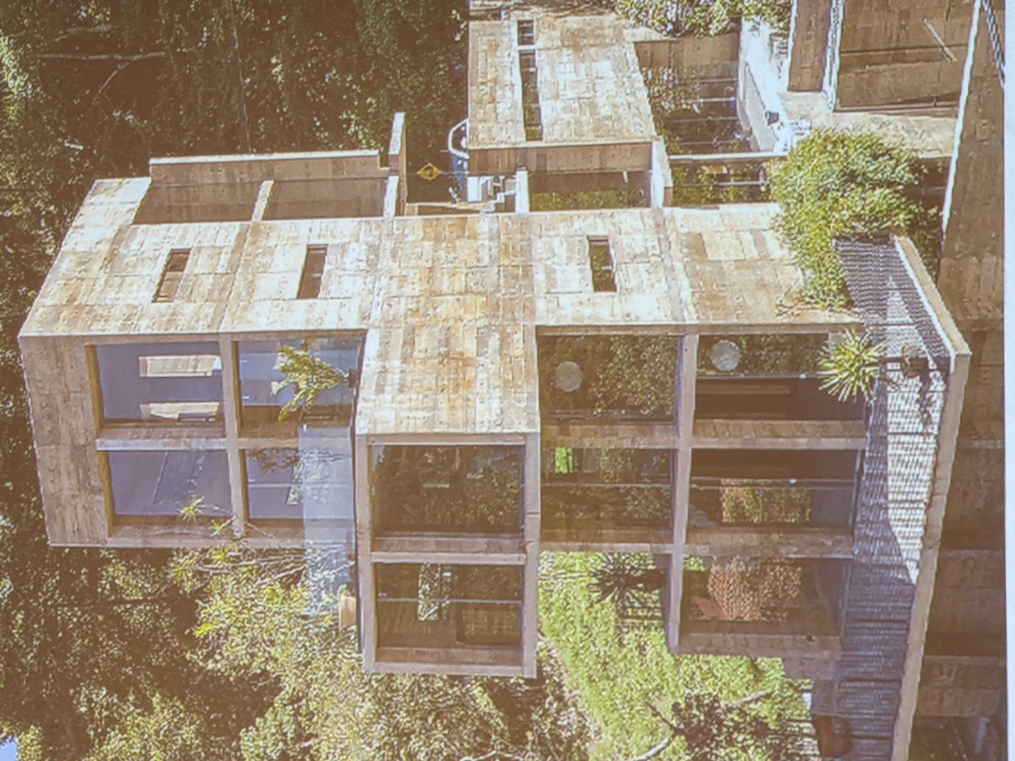 Aerial view of a concrete structure in a wooded area, possibly a building or house, with multiple rectangular compartments filled with greenery. The structure has a layered design, with open spaces allowing vegetation to grow within and around the concrete framework. The location is Unknown, Unknown.