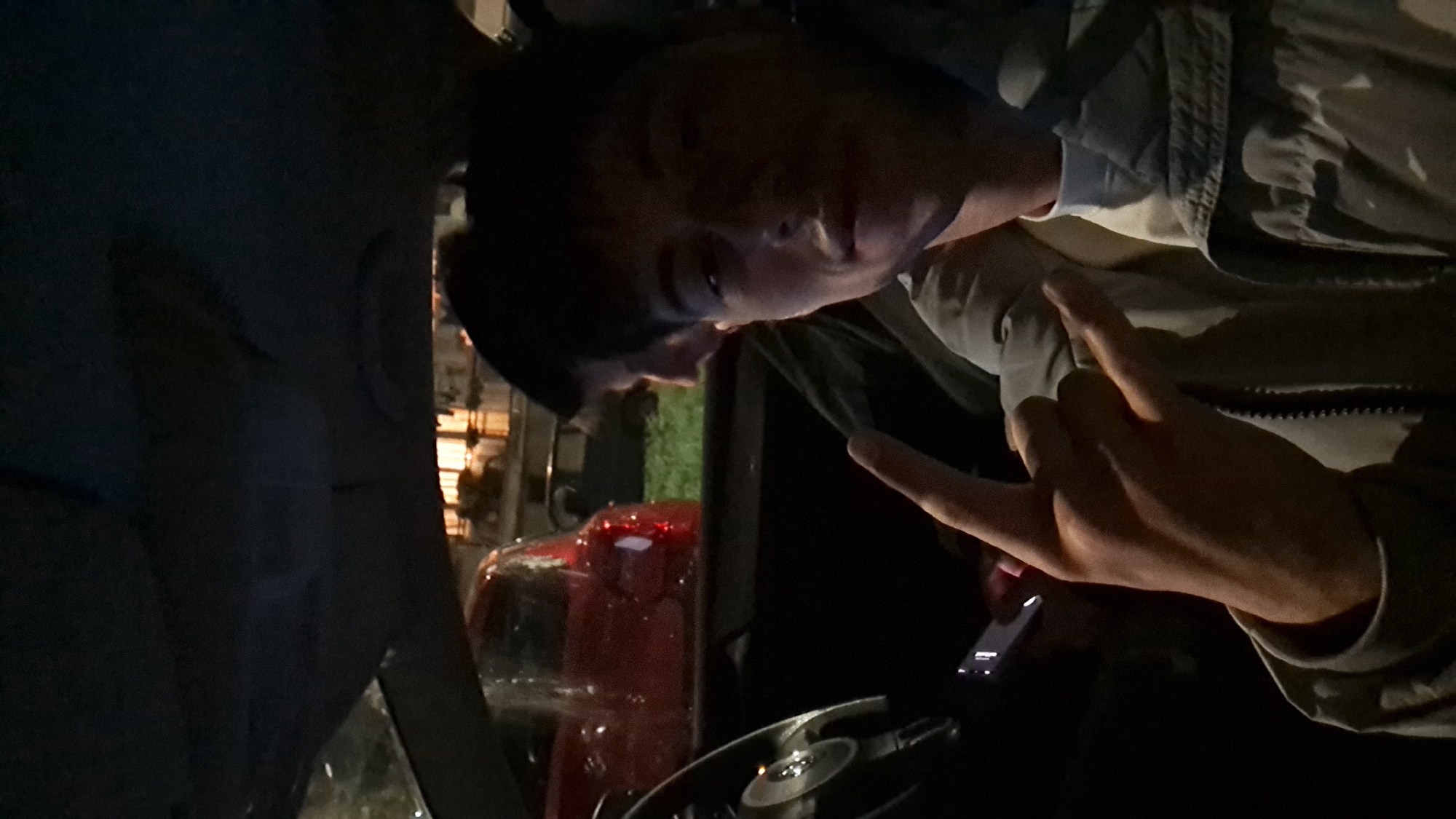 The image appears to be taken inside a car, possibly at night. The person inside is looking at the camera, displaying a hand gesture. A red vehicle can be seen outside the car, and there are faint lights suggestive of a city environment. The location in Burgas, Bulgaria, cannot be determined from the image.
