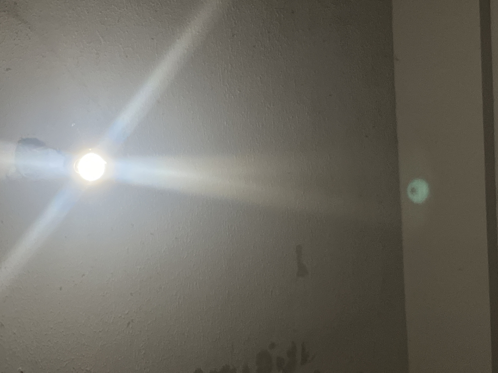 The image is a ceiling with a light fixture, casting beams of light across the textured surface. There are some darker marks or stains on the ceiling, particularly on the left side and in the lower portion. In the bottom right corner, there is a faint circular reflection or glare. The environment appears to be indoors, likely a room with a standard ceiling. The image's origin in Santa Ana, Venezuela, cannot be determined from the visual information alone.