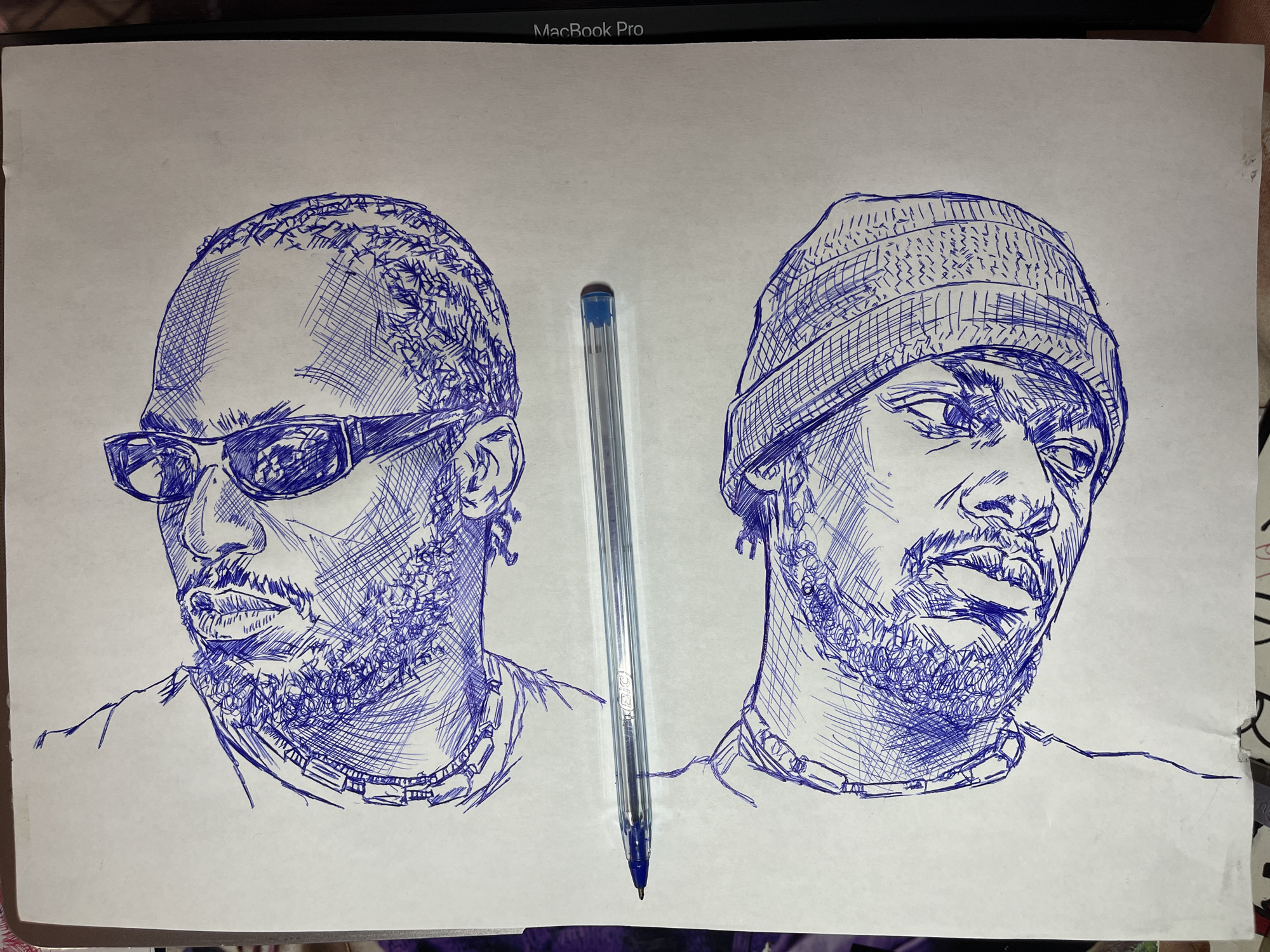 The image is a drawing of two skulls rendered in blue ink on white paper. A blue ballpoint pen is placed horizontally between the two skulls. The drawing style is sketch-like, with cross-hatching and varied line weights used to create form and texture. The skulls appear to be depicted in a dark, somewhat stylized manner, with some details of bone structure and shading. There is no discernible location in the city of Jos, Nigeria mentioned or depicted in this image.