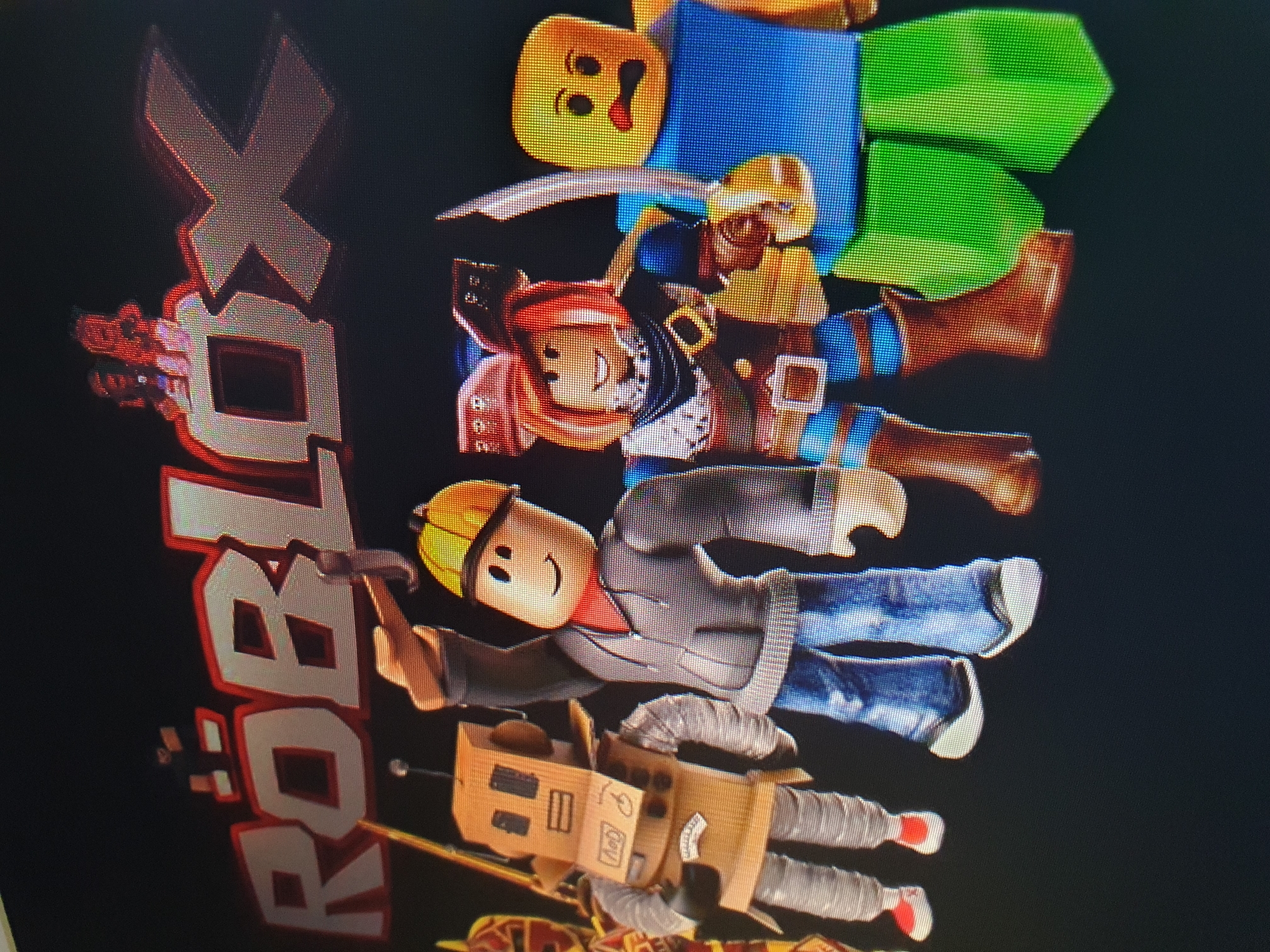 The image is a close-up shot of a screen displaying the Roblox logo and several Roblox characters. The Roblox logo is prominent at the top, with the word "ROBLOX" in large, stylized letters. Below the logo, five Roblox characters are arranged from left to right.
From left to right, the characters are:
1. A character dressed as a robot, with a cardboard box for a head and body, and silver, cylindrical limbs.
2. A character wearing a yellow hard hat, a gray hoodie, and blue jeans, holding a tool.
3. A female character with red hair, wearing a pirate-like outfit with a hat, scarf, and sword.
4. A character with a yellow, blocky head and a blue torso, with green lower body pieces. This character appears to be a "Noob," a common starting character in Roblox.
5. Another character, partially visible on the far right, also with a yellow head.
The background is dark, likely representing a screen or digital environment. There is no indication that this scene is located in Tashkent, Uzbekistan. The image appears to be a photograph of a screen displaying digital content.