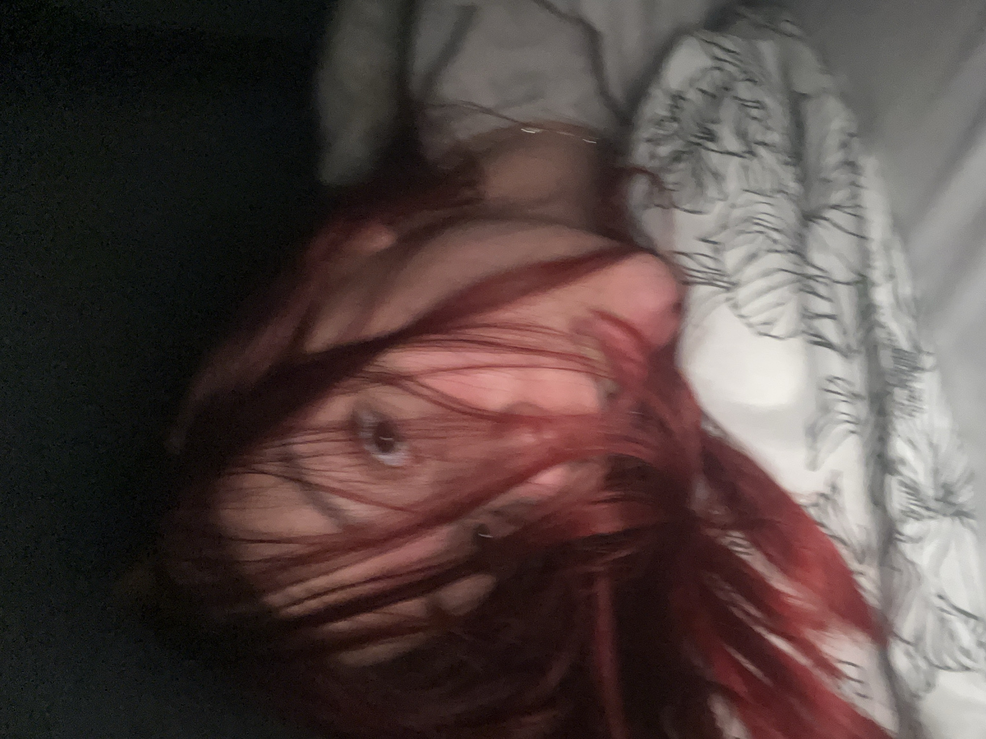 A person with red hair is lying on a bed with a black and white patterned bed sheet. The location is not discernible.