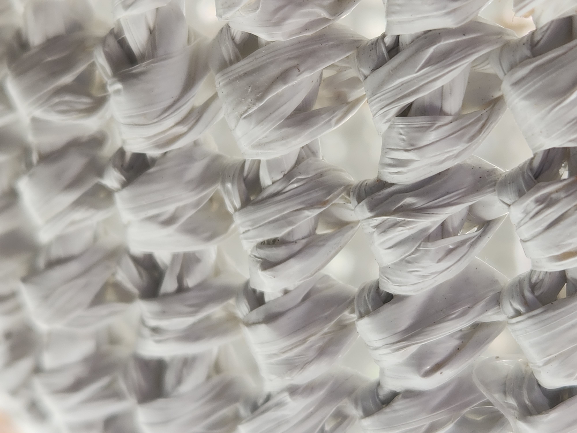 The image shows a close-up, abstract view of a woven white material, possibly made of plastic or raffia. The texture is rough and somewhat irregular, with individual strands visible and forming a crisscross pattern. There are no people, identifiable landmarks, or any contextual elements that would allow for the determination of a specific location within Maitland, United States of America. The scene is entirely focused on the intricate weave of the material itself, with soft, diffused lighting creating subtle shadows and highlights.