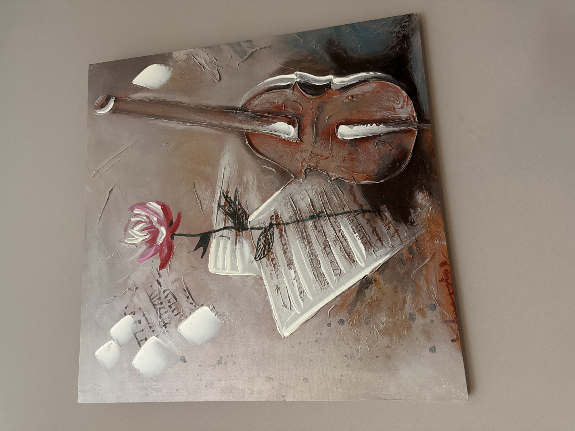 The image displays an oil painting on canvas depicting a still life composition. The artwork features a violin, sheet music, and a pink and white flower with a green stem. The violin is positioned on the right side of the canvas, with its body prominently featured. Sheet music, rendered with thick white impasto strokes, is placed to the left of the violin. A single flower, with vibrant pink petals and white highlights, is positioned centrally, seemingly emerging from the sheet music. Musical notes are faintly visible on the sheet music. The background of the painting is textured in shades of brown, beige, and gray, with occasional splatters of white and darker tones. The painting is hung on a neutral-colored wall, likely in a domestic setting. There is no discernible connection to the city of Targovishte, Bulgaria, in this image.