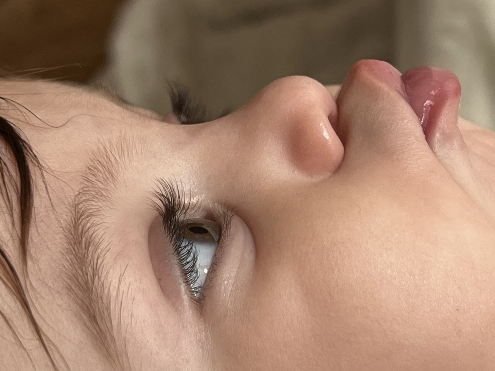 Close-up, side view of a child's face in Elena, Bulgaria. The child's right eye is open and looking upwards, with long eyelashes. The nose and lips are visible. The child's skin is fair. Dark hair is visible near the forehead. The background is blurred and out of focus.