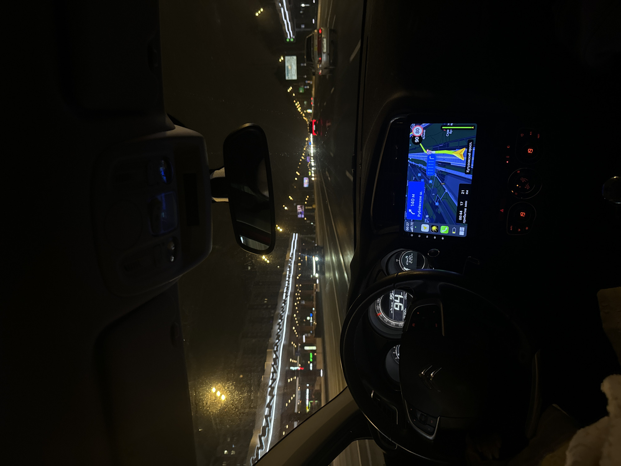 The image shows the view from the driver's seat of a car at night, likely in Moscow, Russia. The car's dashboard is visible, with the speedometer reading 94 km/h and a GPS navigation screen displaying a route. The GPS indicates the car is near Rublyovskoye Shosse (Рублёвское ш.) and Kutuzovsky Prospekt (Кутузовский просп.) with an estimated time of arrival of 17 minutes. The outside view shows a well-lit highway at night, with other cars and street lights visible.