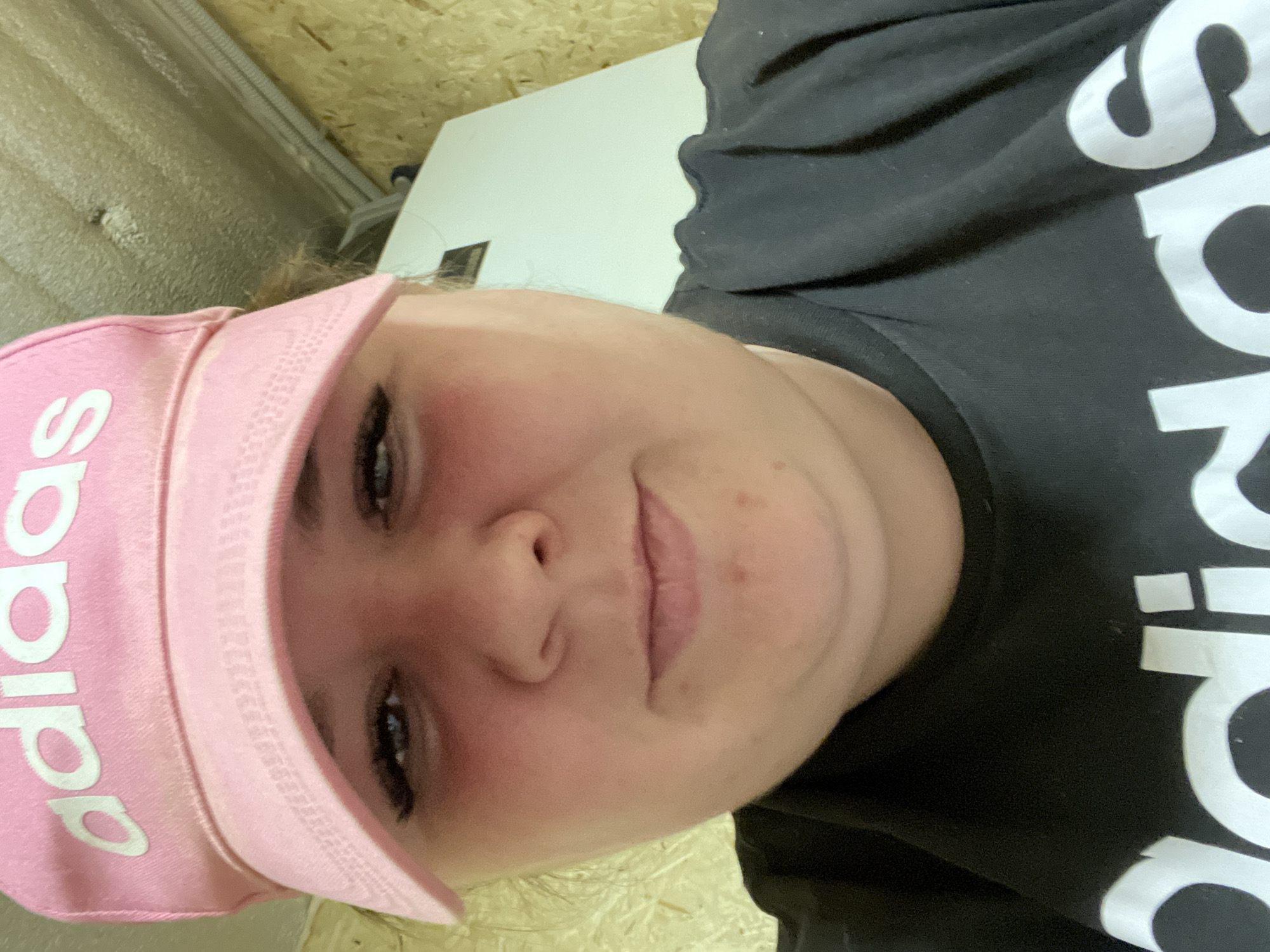 A person wearing a pink Adidas baseball cap and a black Adidas t-shirt is in a room with light-colored walls.