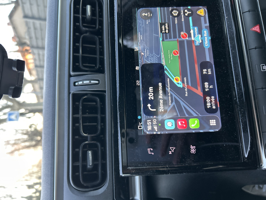 The image shows a car's dashboard with a navigation screen displaying a route. The estimated arrival time is 18:00, with 75 km to go and an estimated travel time of 1 hour and 9 minutes. The current time is 16:51, and the car is currently on "2ème Avenue," 20 meters away from a turn. The temperature is 22 degrees Celsius. The navigation is displaying a route through "Chemin du Charbonnier," and "Rue du Lyonnais". The phone has 5G and is showing multiple apps.