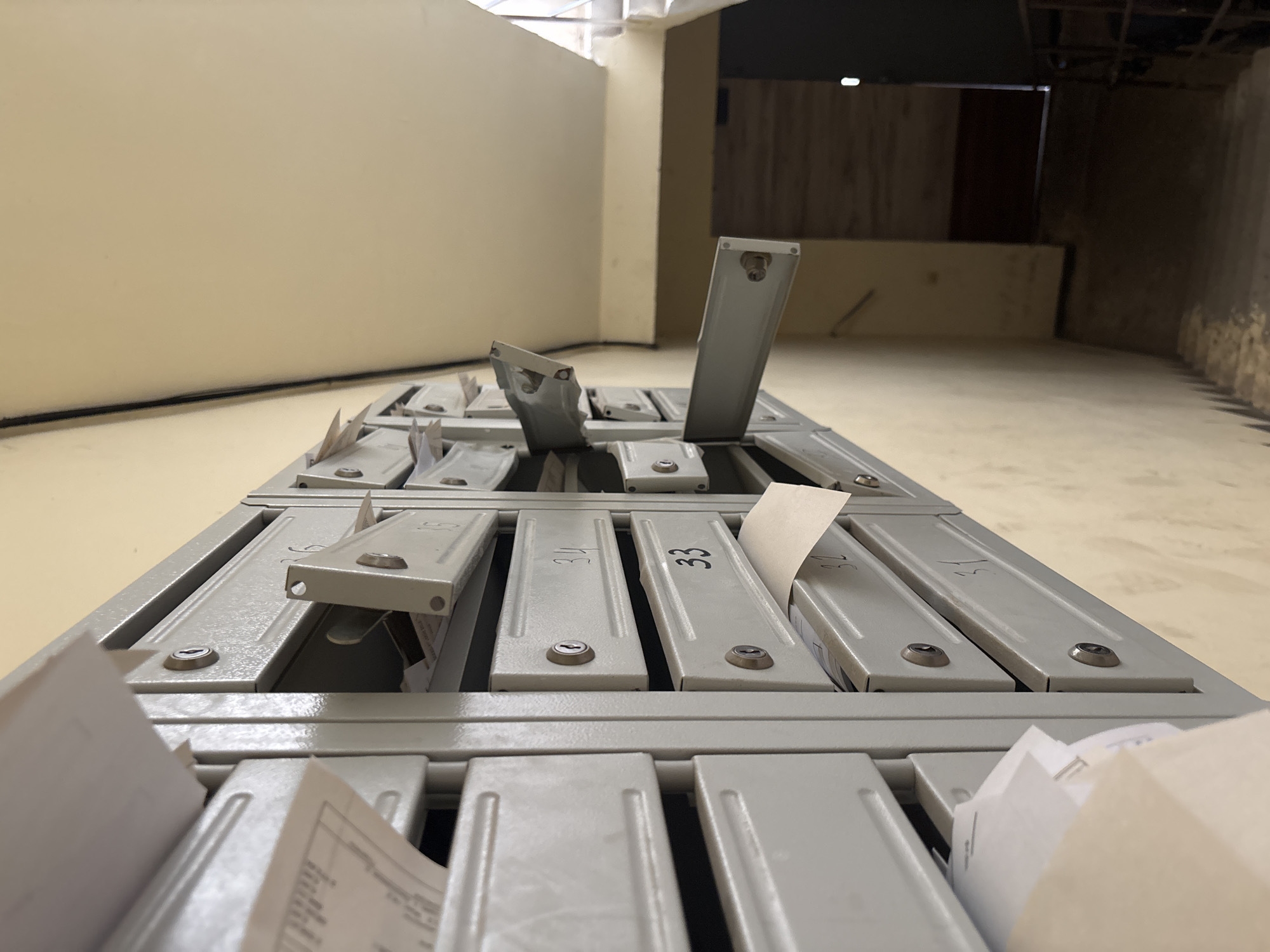 The image shows a row of metal mailboxes, numbered 31, 32, 33, 34, 35, and 36. Some of the mailboxes are closed, while others are slightly ajar, with mail visible inside. The mailboxes are mounted on a light yellow wall, and a cable runs along the top of the wall. To the right, a staircase descends into a dimly lit area. The overall impression is of an apartment building hallway in Krasnodar, Russia.
