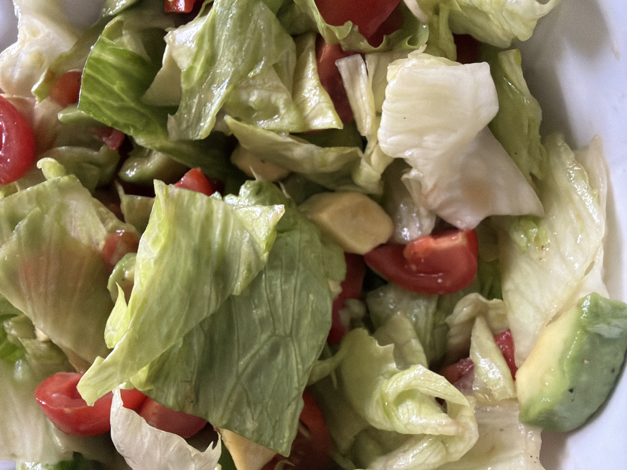 The image shows a close-up view of a salad consisting of lettuce, tomatoes, and avocado. The lettuce leaves appear light green and slightly translucent, and are mixed with halved cherry tomatoes. The avocado is cut into chunks and is positioned on the right side of the frame. The salad is likely in a bowl or container. There is no visible indication of location (Budva, Montenegro or elsewhere).