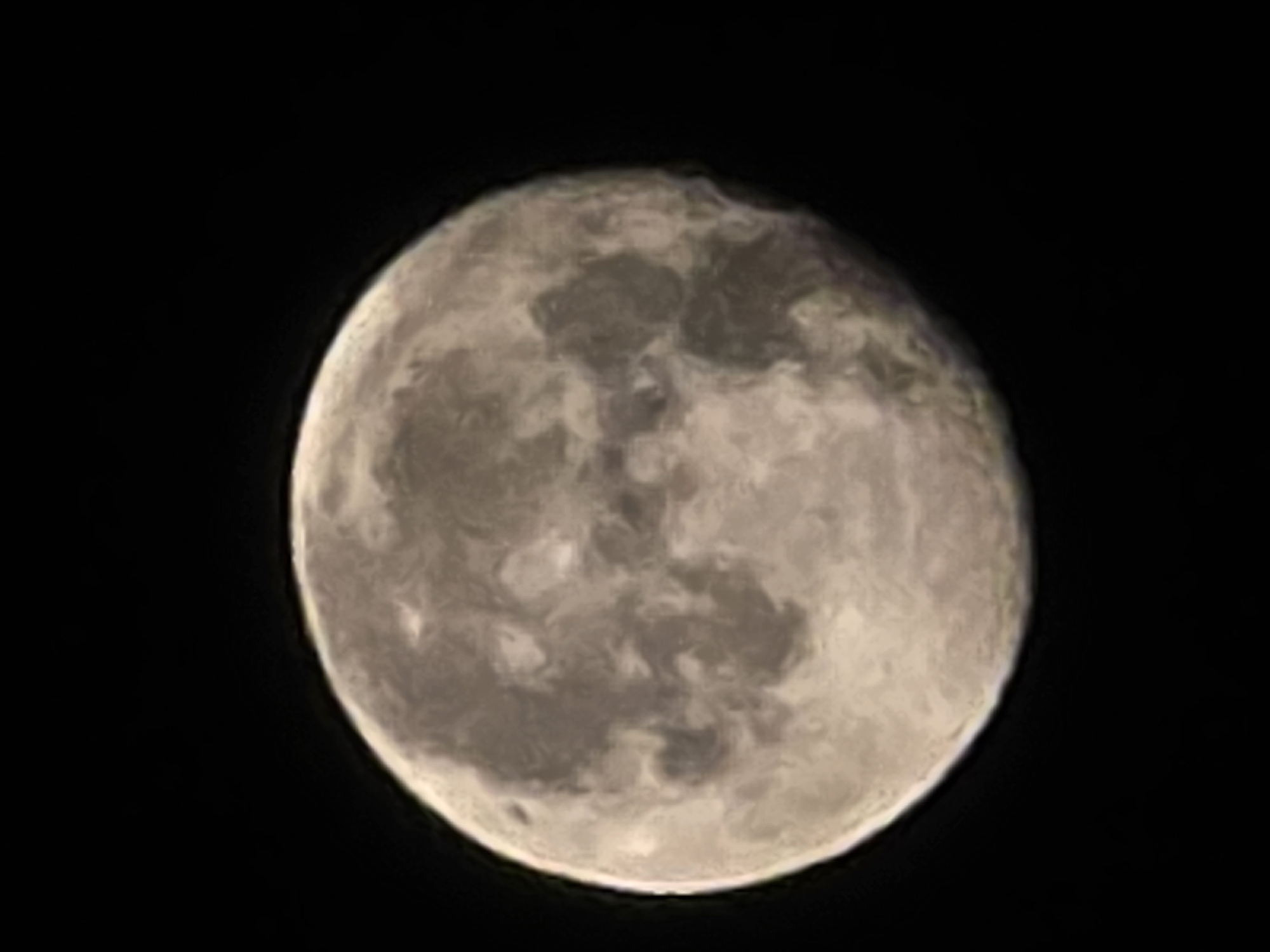 The image shows a full moon against a black sky. The moon has a textured surface with visible craters and darker patches, indicative of lunar maria. The lighting suggests the moon is illuminated from the right. There are no people, buildings, or any other objects visible in the image, nor any indication of a city or specific location. The image is a close-up shot of the moon in space.