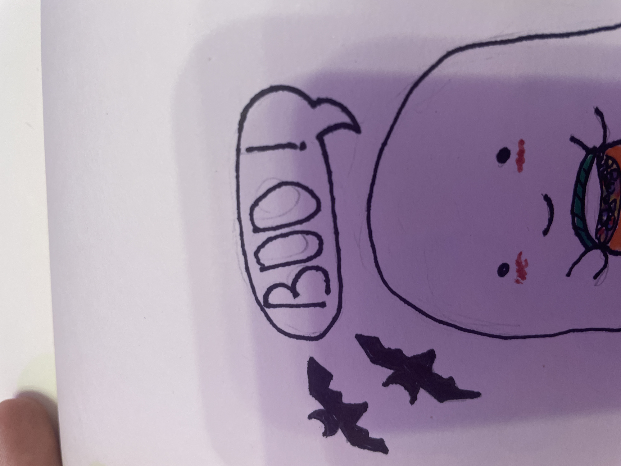 The image shows a close-up, slightly angled, top-down view of a drawing on white paper, with a purple tint from lighting. The drawing features a cartoon ghost with blush marks on its cheeks and a smile. It is holding a candy bucket, which is partially visible. Above the ghost, there is a speech bubble containing the word "BOO!" in bold black letters. To the left of the speech bubble, two black silhouettes of bats are flying. The background is the plain white paper. There are no discernible elements of Saint Petersburg, Russia, or any specific city location within the image.