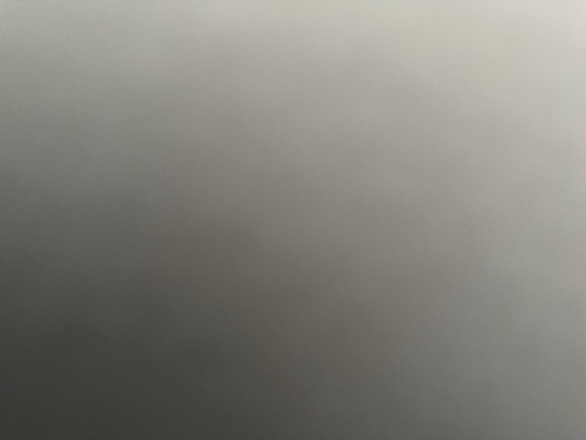 This is a still image with a gradient of grey tones, ranging from a dark grey in the bottom left corner to a light grey or off-white in the top right corner. There are no discernible subjects, objects, or scenes visible. The image is a smooth gradient with subtle texture, possibly from a matte surface. There are no visible details related to time of day, weather, location, or emotions. No text is present in the image. The overall impression is one of a textured, abstract background.