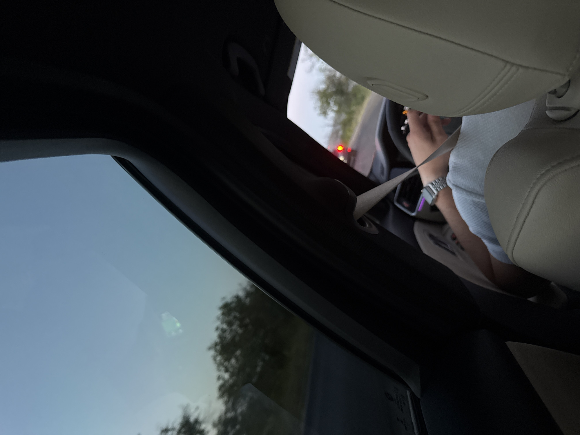 The image shows the interior of a car looking forward through the windshield and sunroof. The sky is a pale blue, with some trees visible in the distance. The car appears to be on a road, with another car visible in front. The driver's hands are on the steering wheel, and a seatbelt is visible across their chest. The interior of the car is upholstered in light-colored leather. The image does not provide enough information to determine the specific location in Fundul Galbenei, Moldova.