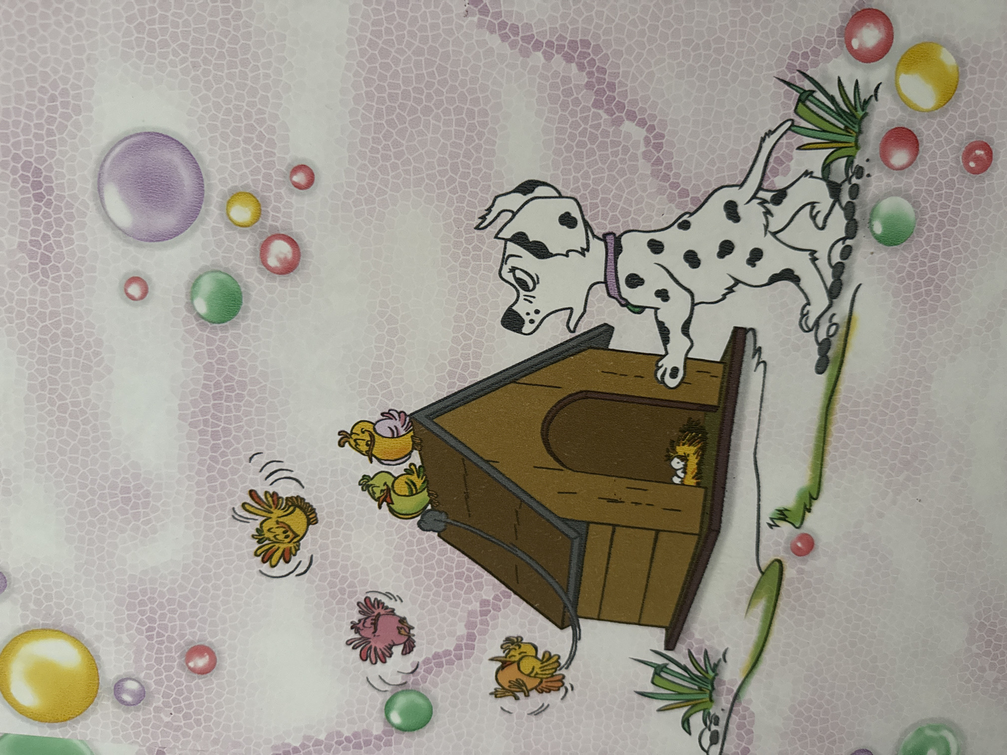 This image depicts a cartoon scene with a Dalmatian dog, a doghouse, and several cartoon birds. The dog is standing on its hind legs, looking up and to the right with its mouth open, as if barking or reacting to something. The doghouse is brown with a dark roof. On top of the doghouse, two yellow and green birds are perched. To the left of the doghouse, several other birds are depicted in motion: a pink bird is flying, and a yellow bird is also in flight, seemingly attached to the doghouse by a thin string. Inside the doghouse opening, a nest with three eggs is visible. The background features a light pink, textured pattern resembling tiny cells, with scattered colored circles that appear to be bubbles or marbles in shades of yellow, green, pink, and purple. The ground is depicted with green grass and a gray, wavy line. The overall style is illustrative and whimsical.
There is no information within the image that provides context for its location in the city of Bălți, Moldova.