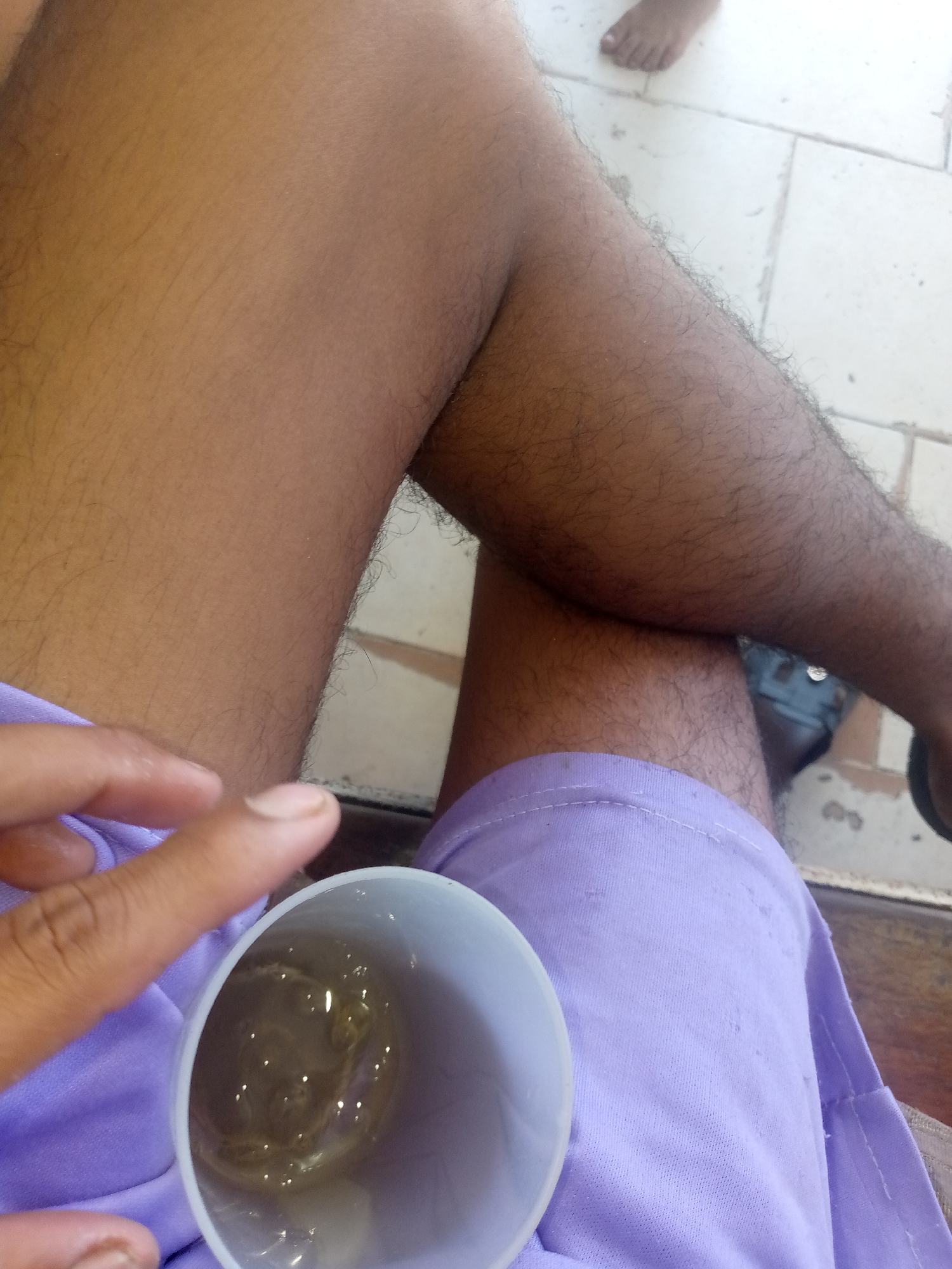 The media file is a close-up shot focused on a person's legs and a cup. The subjects are a person's legs, clothed in light purple fabric, and a white cup containing a light-colored liquid. The person appears to be sitting, as their legs are bent. A hand, with fingers partially visible, is near the cup, suggesting the person is holding or interacting with it.
The setting appears to be outdoors or in a well-lit indoor space with tiled flooring visible in the background. The tiles are a light color, possibly white or beige, and are arranged in a grid pattern. There's a hint of another person's foot in the upper right corner, also on the tiled floor.
The activity taking place is unclear, but the presence of the cup and the hand suggests a moment of rest or refreshment. The lighting is bright, indicating it could be daytime. No specific weather conditions are discernible. There are no visible text elements in the image. The overall mood is casual and relaxed.
