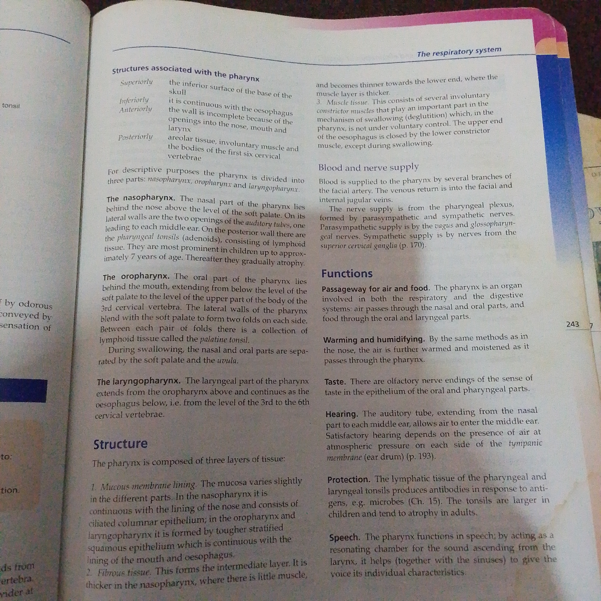 The media file is a photograph of an open book, likely a textbook or educational material. The page displays text with headings and subheadings, indicating a subject related to human anatomy or physiology, specifically focusing on the "respiratory system" and the "pharynx."
**Subjects:** The primary subjects are the text and the printed layout of the book itself. There are no people, objects, or a discernible scene or setting beyond that of a book on a surface.
**Activity or Event:** The "activity" is informational. The book is presenting educational content about the pharynx, its structure, blood and nerve supply, and functions.
**Notable Details:**
* **Text:** Visible text includes anatomical terms such as "pharynx," "nasopharynx," "oropharynx," "laryngopharynx," "tonsils," "auditory tubes," "oesophagus," "larynx," and "swallowing." There are also descriptions of tissues ("ciliated columnar epithelium," "stratified squamous epithelium," "fibrous tissue," "muscle tissue") and physiological processes ("blood and nerve supply," "functions").
* **Page Number:** The page number "243" is visible, along with a smaller digit "7" which might be a chapter or section indicator.
* **Book Structure:** The page shows the typical layout of a textbook, with a title at the top ("The respiratory system"), main headings ("Structures associated with the pharynx," "Structure," "Blood and nerve supply," "Functions"), and bulleted or numbered lists.
* **Visual Cues:** The colors of the page are typical of printed paper, with black text on a white background. The edge of the page has a pink and blue binding, suggesting it is part of a larger bound volume.
**Location Context:** The provided location context of "Jalingo, Nigeria" is not directly reflected in the image itself. The image shows a generic educational book and provides no visual cues to its specific geographical location. The content is universally anatomical and physiological.