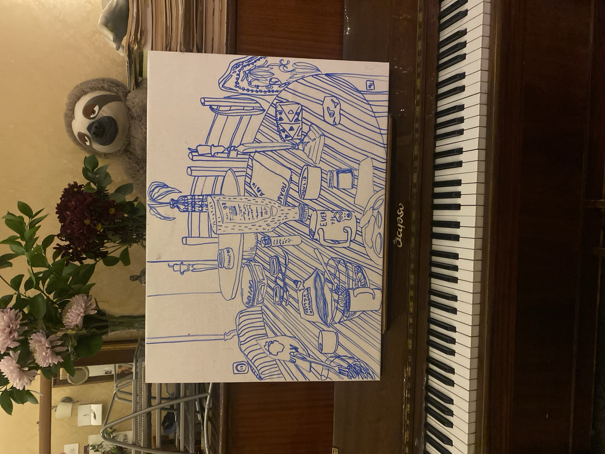 The image, rotated 90 degrees counter-clockwise, depicts an indoor scene, likely in Moscow, Russia. The central element is a white canvas featuring a detailed blue line drawing. This drawing illustrates a cluttered surface, resembling a table or desk, filled with various objects. Recognizable items in the drawing include several bottles, one labeled "I LOVE YOU" and another with Cyrillic text "ЗАВИНЧУ". Also visible are cups, dice, a plate, a small fan, and what appears to be a partially visible pack of "LUCKIES" cigarettes. Additional text "MONOLID" and "EVER" can be seen within the drawing.
To the right of the canvas, a section of a piano keyboard is prominently displayed, showing numerous white and black keys. A partial inscription, possibly "Seydel", is visible on the wooden frame above the keys.
On the left side of the frame, a plush toy sloth with brown eyes and a friendly expression peeks in from the top. Below the sloth and to the left of the canvas, a clear vase holds a bouquet of flowers, consisting of light pink chrysanthemums and darker red blooms. In the background, a mirror reflects part of the room, including a metallic mesh organizer and other small items. A stack of books or papers is partially visible behind the sloth.
The scene captures a still life arrangement within a personal and lived-in environment. No people are present, and no specific event is actively taking place. The drawing itself appears to be an artistic rendition of everyday objects.