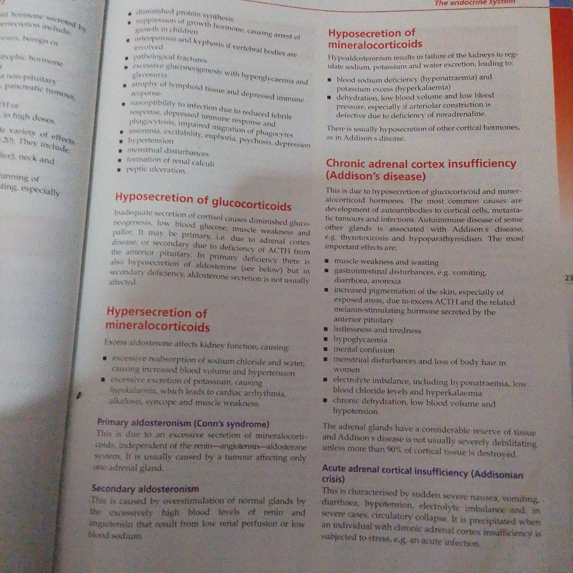 The image is a close-up of a textbook page. The page is white with black text, organized into paragraphs and bulleted lists, and highlighted headings in red. The text discusses endocrine system disorders, specifically focusing on the adrenal glands and their hormones like glucocorticoids and mineralocorticoids. Several conditions are detailed, including hyposecretion and hypersecretion of these hormones, leading to diseases like Addison's disease and Cushing's syndrome, as well as primary and secondary aldosteronism. There are no people, objects, or scene details visible in the image, other than the book itself. The text is purely informational and scientific. The only visible numbering is the page number "23" in the bottom right corner. There are no environmental cues to suggest a specific time of day, weather, or location, beyond it being a page from an educational book. The tone of the text is formal and objective, typical of an academic or medical textbook.