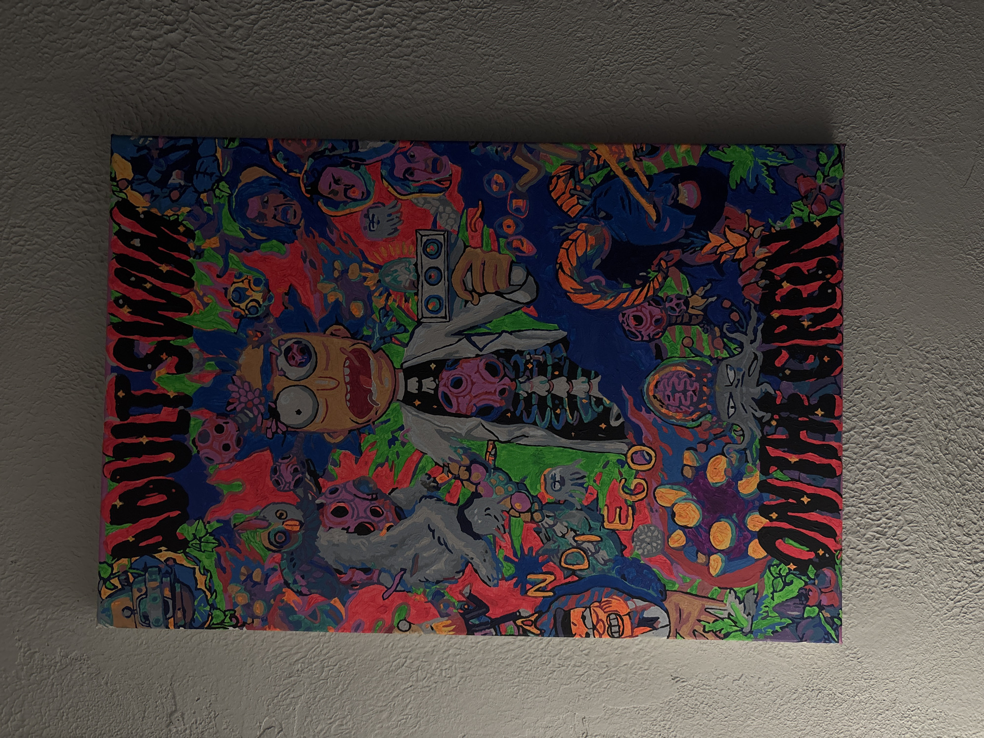 The image shows a painting hanging on a textured wall. The painting features a cartoon character resembling Rick Sanchez from the "Rick and Morty" series, surrounded by abstract and psychedelic imagery. The words "ADULT" and "DEGENERATE" are written on the sides of the painting in a stylized font. The overall color palette is vibrant, with shades of blue, red, green, and orange dominating the composition. The painting is centrally positioned and appears to be a homemade art piece. There is no evidence of Zheleznogorsk, Russia in the image.
