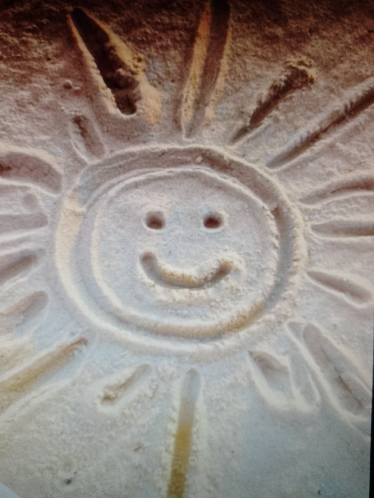 A depiction of a sun with a smiling face, carved into what appears to be sand. The location is unknown.