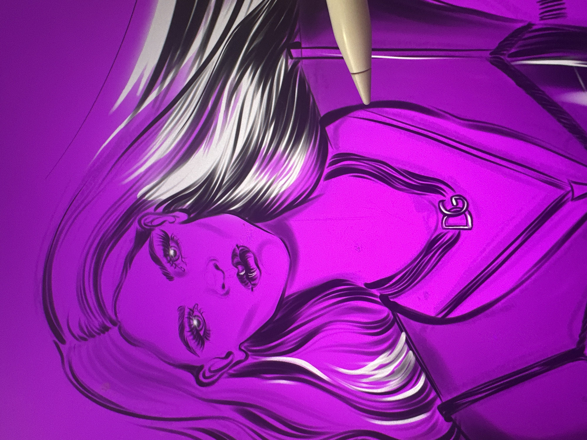 The image is a digital illustration of a woman's face and upper body, rendered in various shades of pink and purple. The style is stylized, with bold outlines and dramatic highlights. The woman has long, flowing hair that appears to be dark with light streaks. Her eyes are large and expressive, with prominent eyelashes and bright, reflective pupils. Her lips are full and painted, with a detailed texture. She is wearing a necklace with the letters "DG" as a pendant. She is also depicted wearing a jacket or blazer with a V-neckline. A stylus, likely used for digital art creation, is visible in the lower right corner, positioned as if it is interacting with the artwork. The background is a solid, bright pink. The overall impression is a glamorous and artistic portrait. The location is not specified.