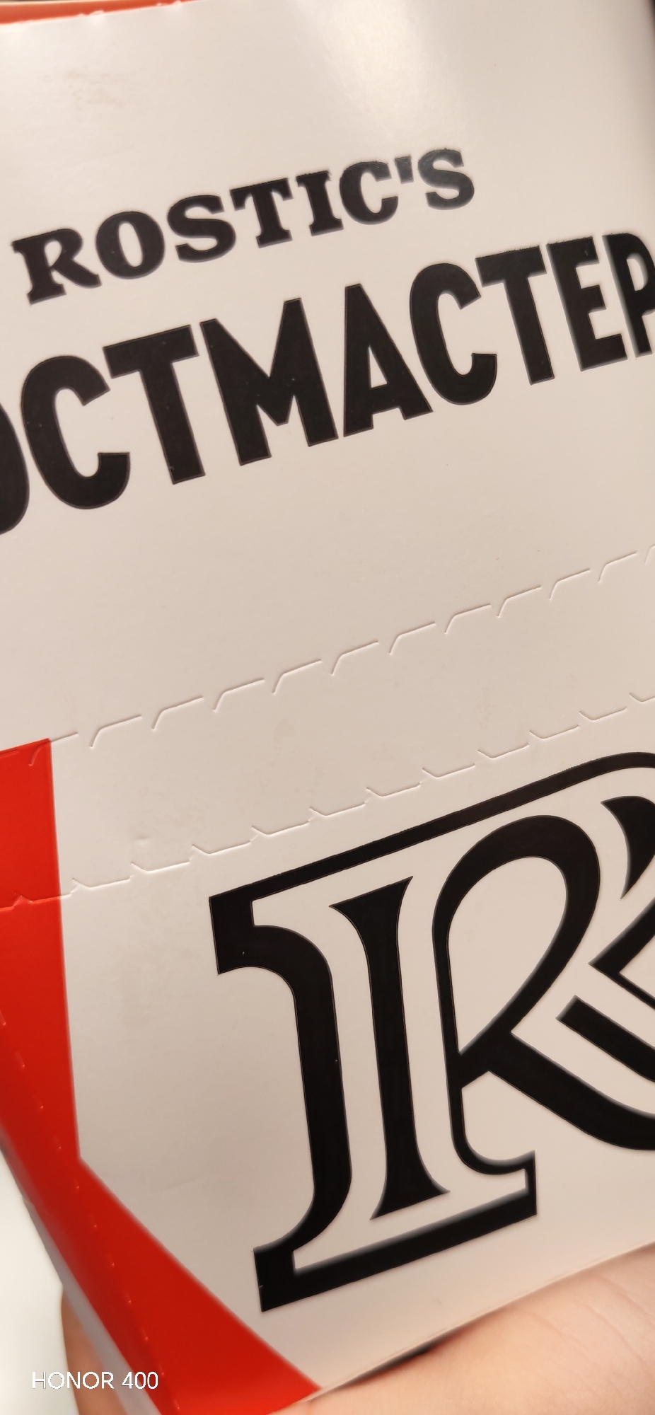The image shows a portion of a package labeled "ROSTIC'S OCTMASTER". Beneath this is a line of perforations, below which appears a partial black stylized "R" logo. The package has a red trim. The text "HONOR 400" appears in the lower left corner. The location, Izhevsk, Russia, is not discernible from the image.