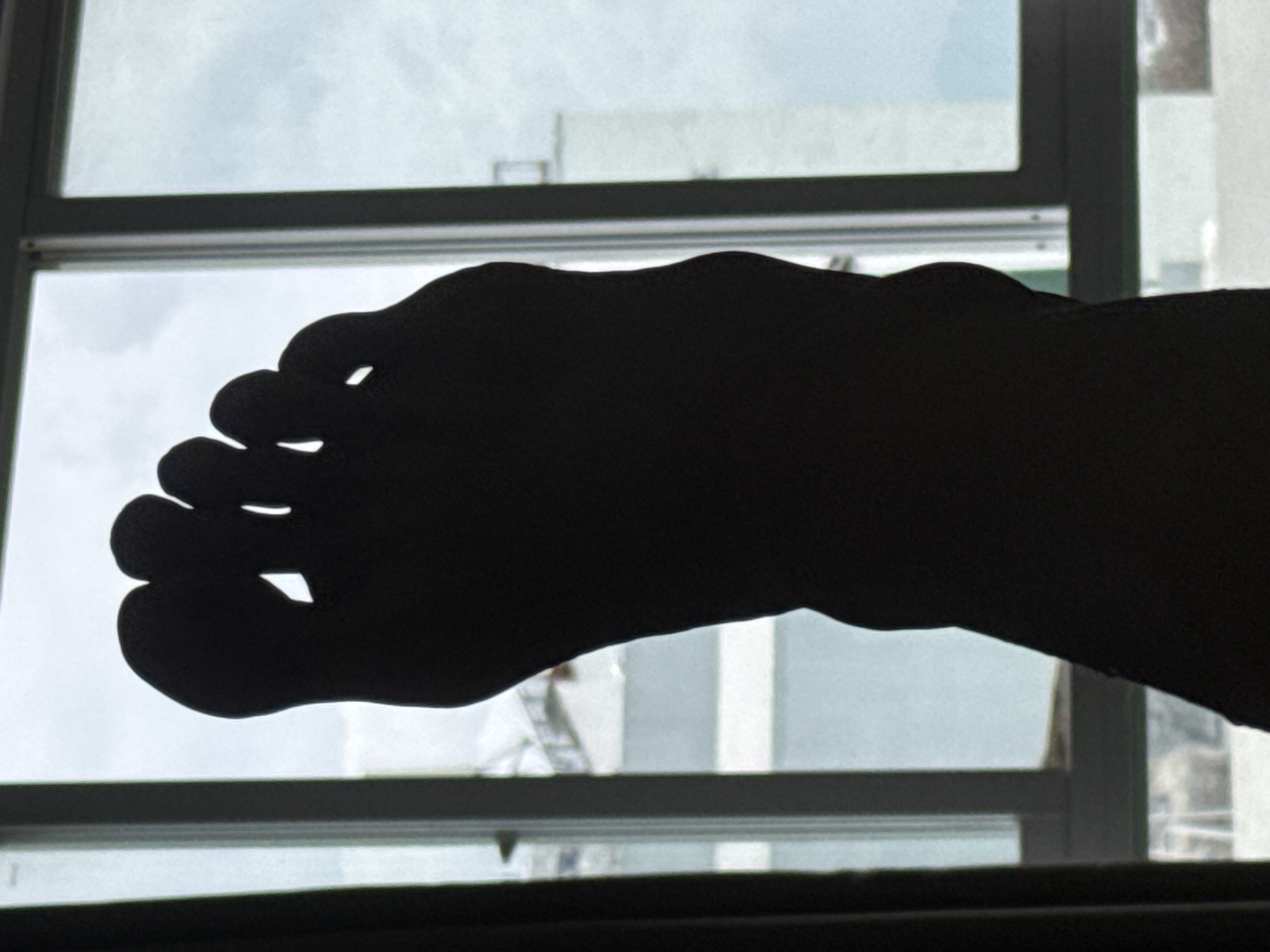 The image depicts a silhouette of a human foot against a window. The background visible through the window includes the sky and buildings, suggesting an urban environment. Based on the query, this scene is supposedly located in Bac Nha Trang Ward, Vietnam, although this is not explicitly verifiable from the image itself.