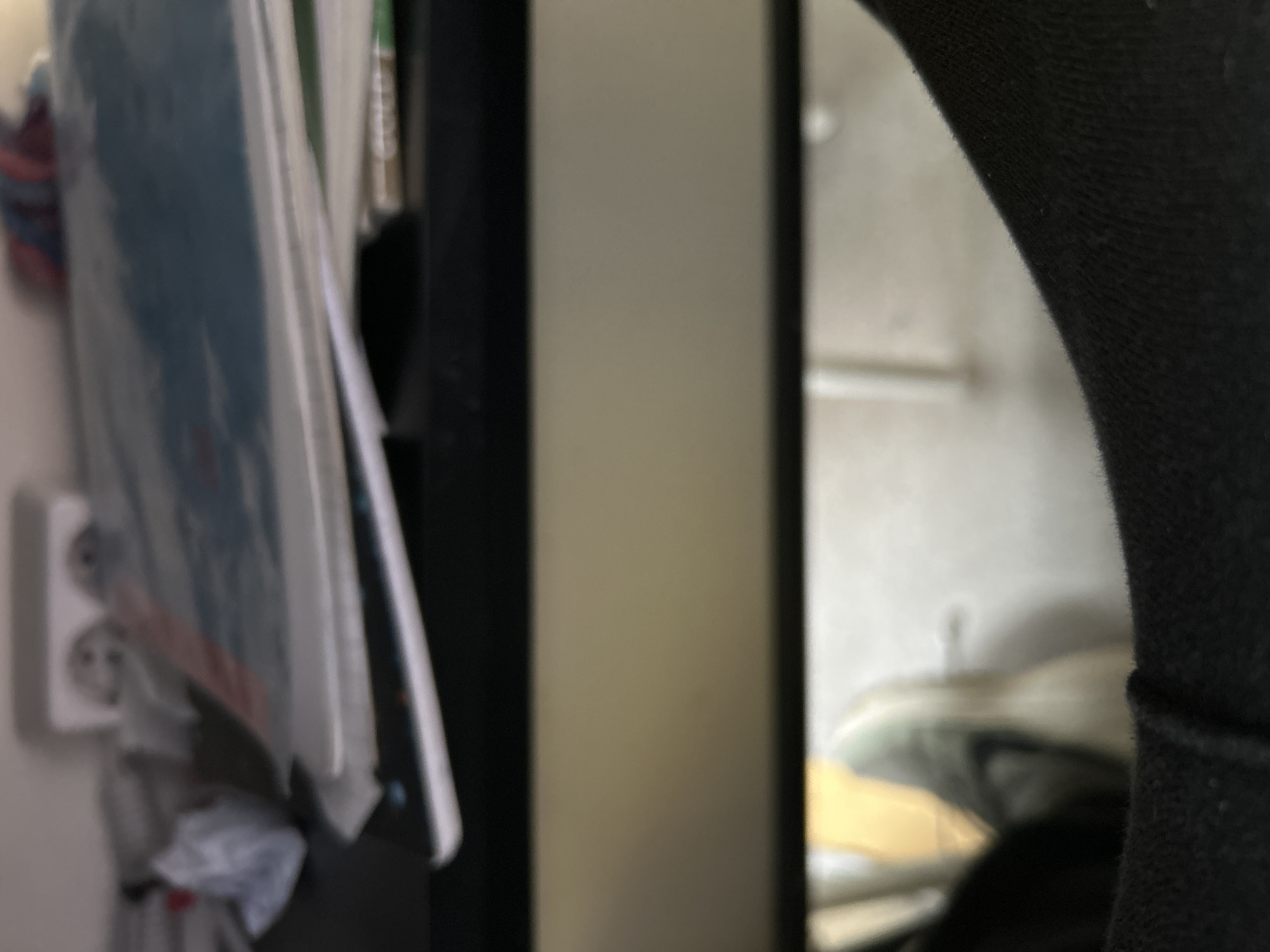 The image depicts a close-up view of an interior space. The foreground contains an electrical outlet, various papers and books, and a black object. The background is blurred, but shows a white wall with a horizontal bar and indistinct shapes. Based on the information available, it is impossible to determine the location as Burgas, Bulgaria.