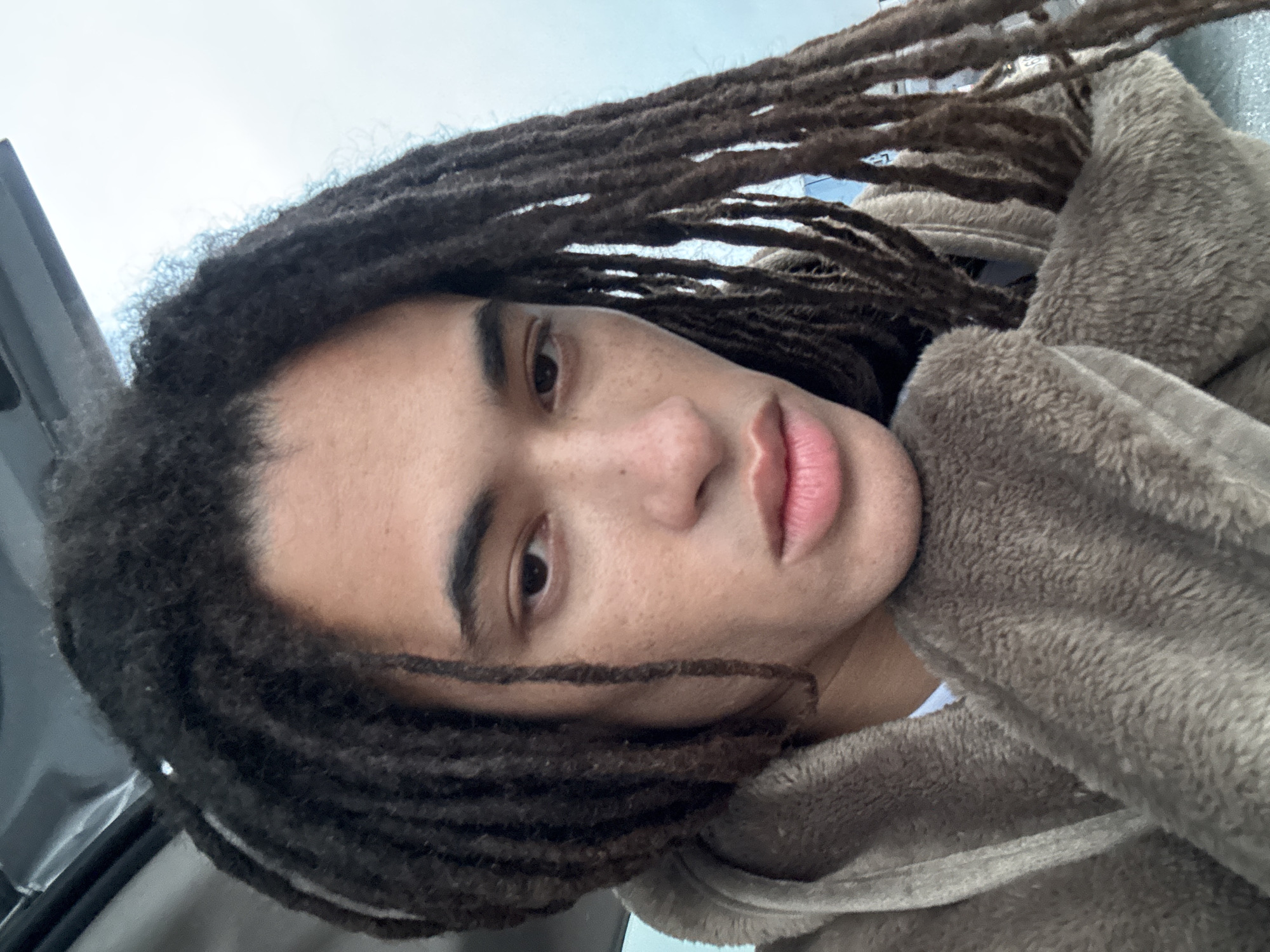 A person with dark dreadlocks is partially seen. The person is wearing a brown, soft, plush garment. The location in Teguise, Spain cannot be determined from the image.