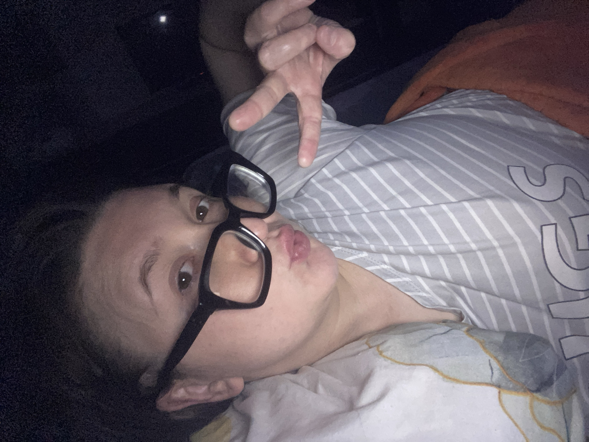 A woman is lying down, wearing glasses and a striped shirt, and making a hand gesture. The location appears to be indoors. The information to ascertain its place is absent, thus location Chaikovsky, Russia cannot be verified.