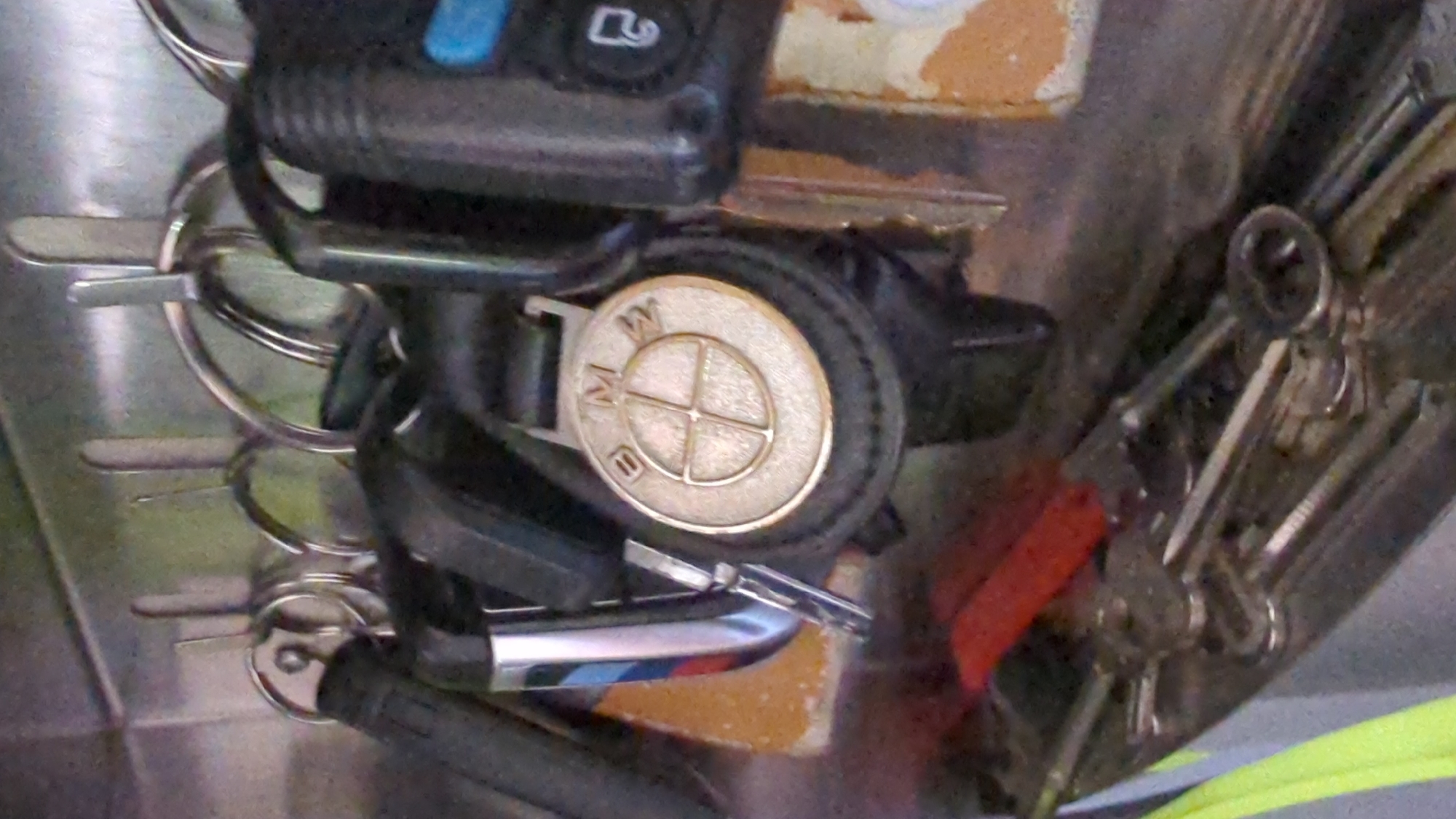 A keychain with a BMW emblem is attached to a hook on a metal key rack. Multiple keys are on the keychain, and other keys are also hanging on the rack. The background appears to be a shelf or cabinet. The scene is indoors and likely a residential or commercial space. The image is of moderate resolution and appears to be a close-up shot of the keychain and keys. There is no indication of the location in Kløfta, Norway.