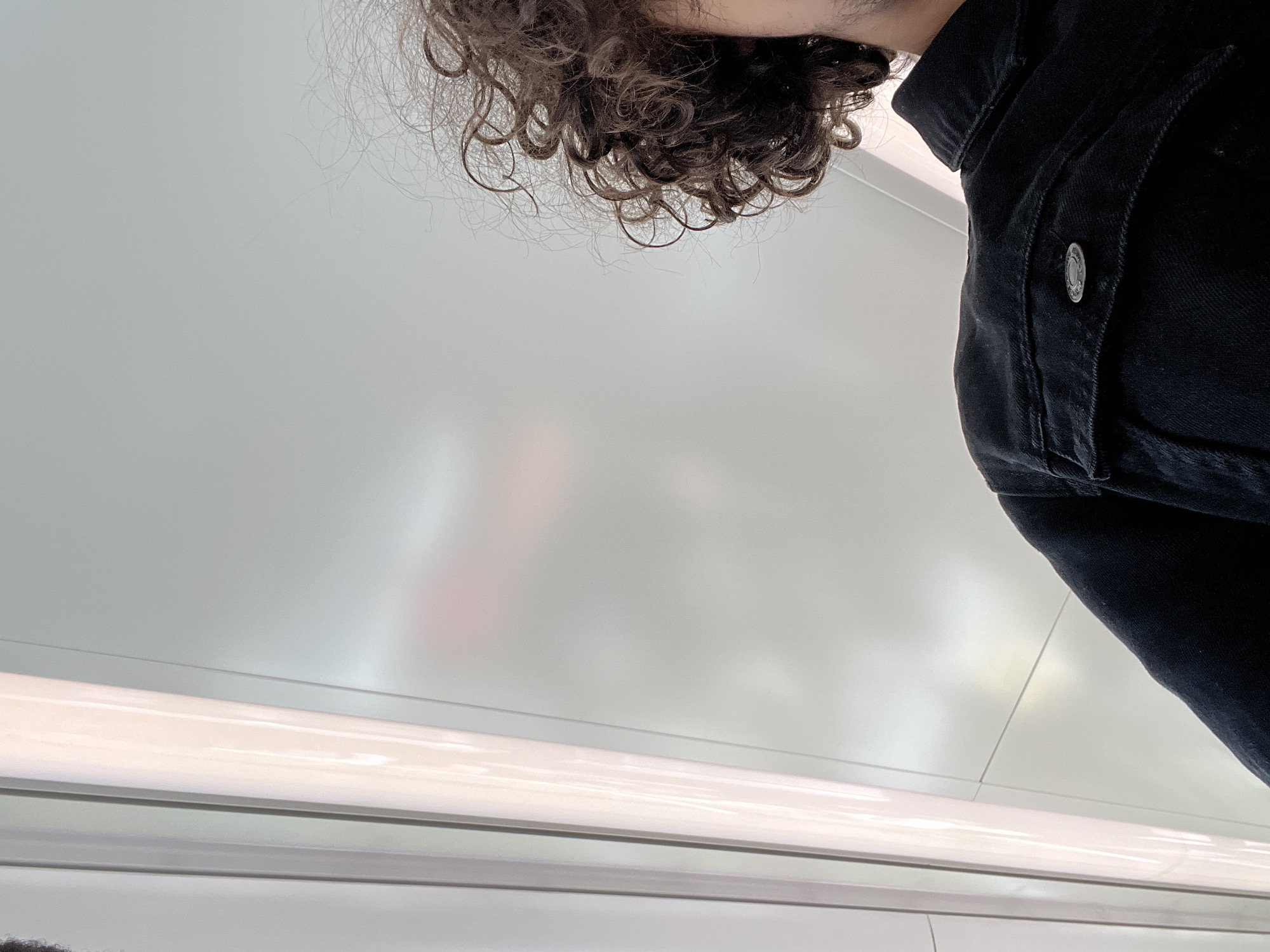 The photo is taken from a low angle, looking up at a person with curly hair and wearing a black denim jacket. The setting appears to be the interior of a train or tram, evidenced by the white ceiling panels and linear lighting fixture. There are no other discernible people or objects in the visible background. Without additional visual clues or context, specifying the exact location within Strasbourg is not possible.
