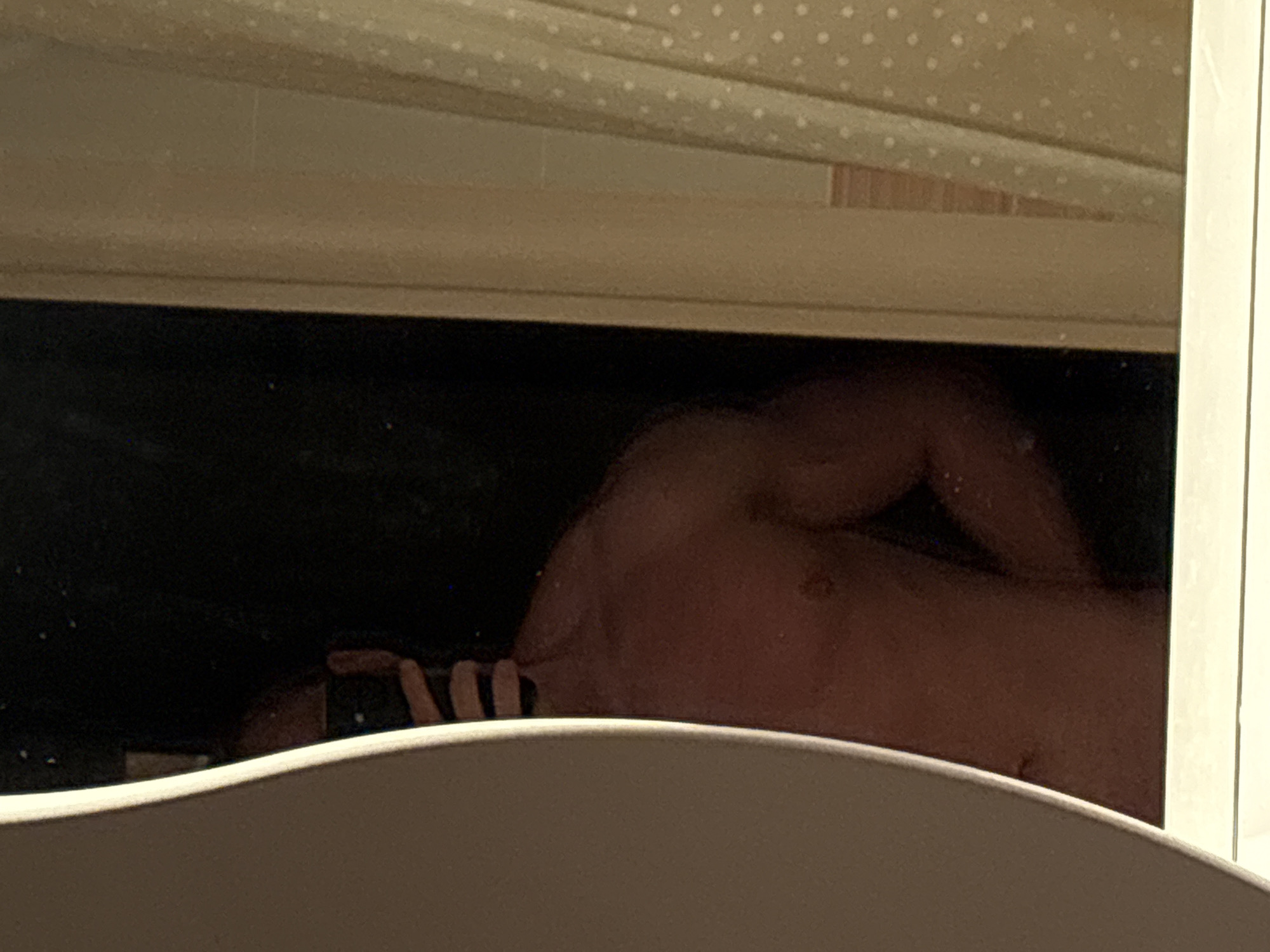 A shirtless individual with a phone is reflected in a bathroom mirror. The location is unknown; there is no indication it is Chaikovsky, Russia. The view is partially obscured by the bathroom sink.
