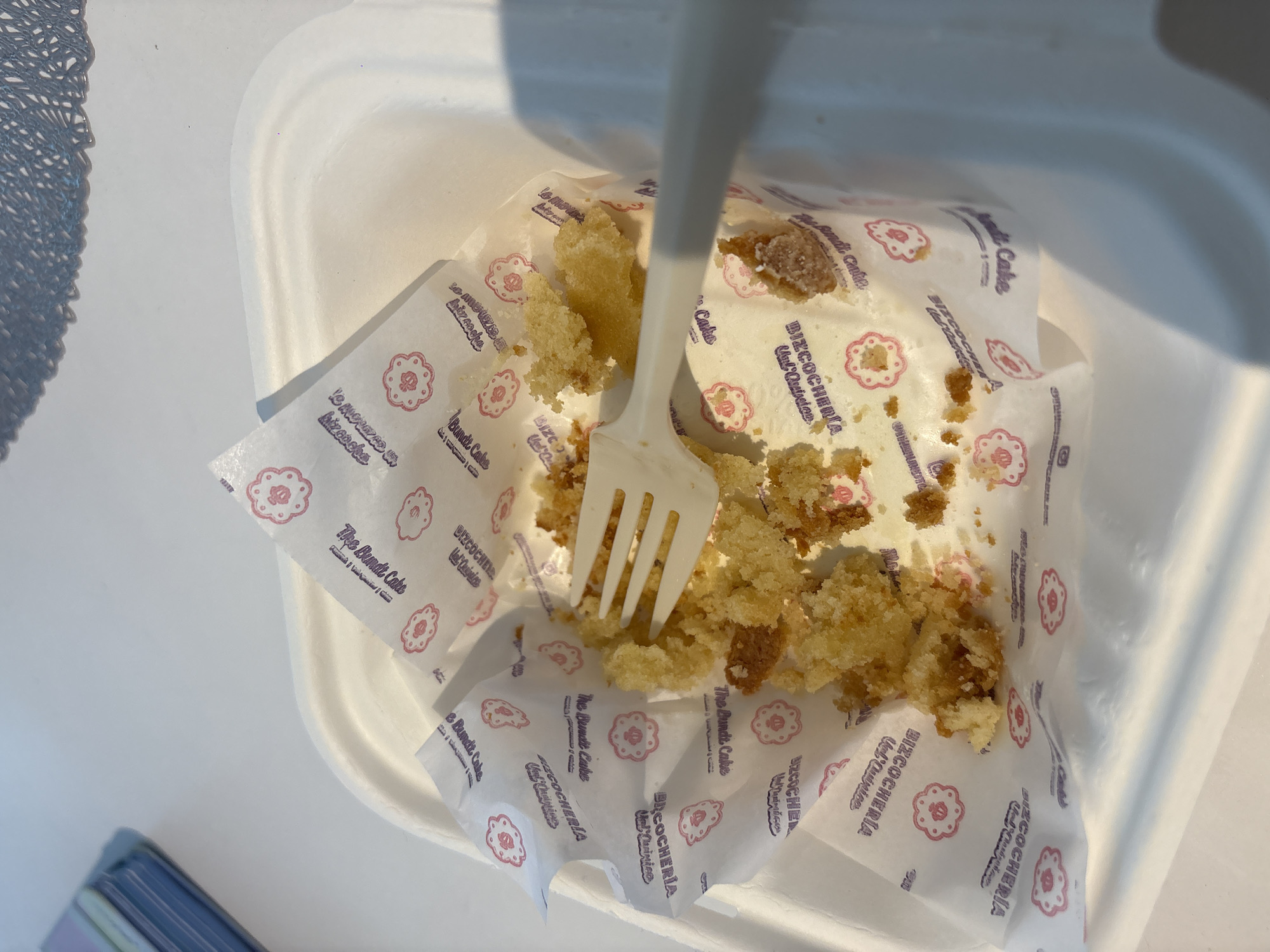 The image shows the remnants of a cake inside a white container with a white plastic fork stuck in it. The cake crumbs are on a piece of branded paper labeled "The Bundt Cake" and "BIZCOCHERIA, Val'Quirico." The location can be identified as Val'Quirico, a tourist destination in Puebla, Mexico.