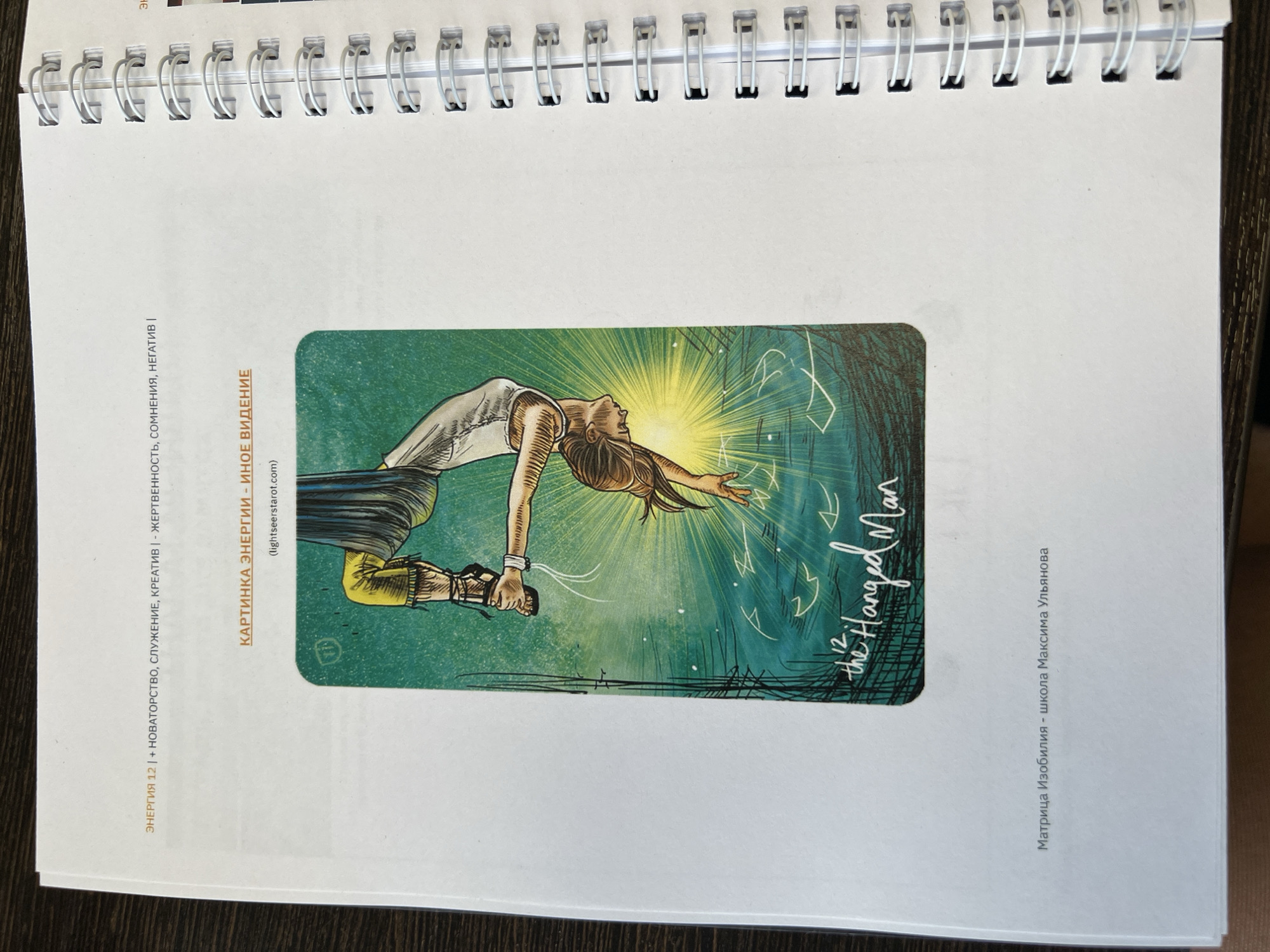 The image shows an open notebook with a spiral binding. The page displays an illustration of "The Hanged Man" tarot card from the Light Seer's Tarot deck. Text in Russian surrounds the image, including "ЭНЕРГИЯ 12," "КАРТИНКА ЭНЕРГИИ - ИНОЕ ВИДЕНИЕ," and "(lightseerstarot.com)". The image is a scan of a page that's likely part of a larger work about the tarot, possibly by a Russian author, Maxim Ulyanov. The location, Perm, Russia is not evident from the image.