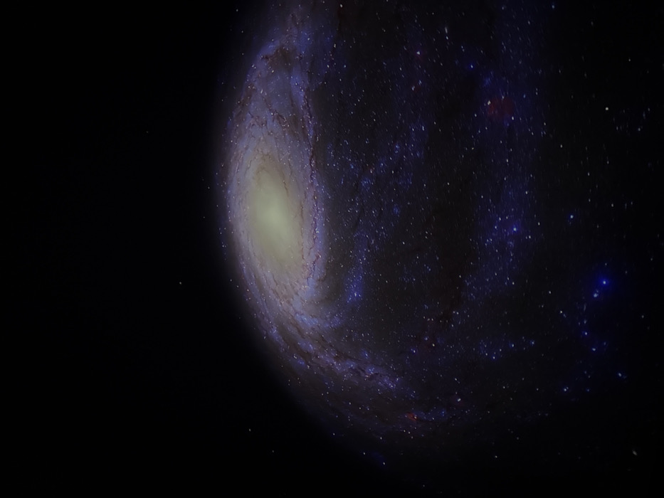 The image displays a prominent spiral galaxy, characterized by a luminous, yellowish-white central core from which intricate spiral arms, adorned with bright blue and white star clusters and dark lanes of interstellar dust, coil outward against the deep black canvas of space. The environment is purely cosmic, featuring sparsely scattered individual stars across the background. This scene is devoid of any discernible terrestrial features, human subjects, man-made objects, or any actions or interactions. The visual content presented is astronomical in nature, providing no identifying markers for a specific location within the city of Canela, Brazil.