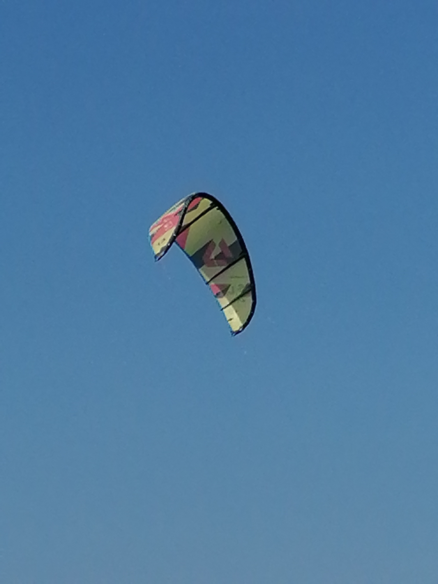 A kiteboarding kite is in the air against a clear blue sky. The kite is green with black and pink patterned details. The exact location is not discernible, but it is likely in Nha Trang Ward, Vietnam, given the prompt. The sky is cloudless. No people are visible in the frame.
